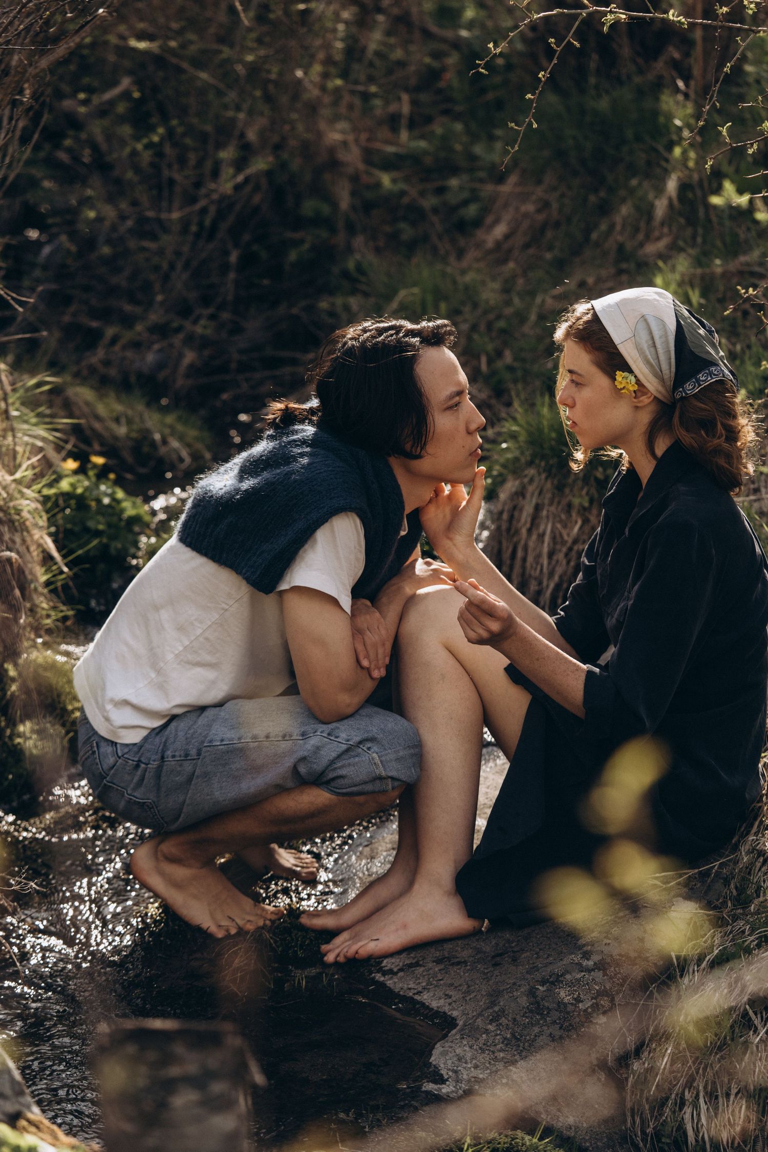 A couple shares tender moments while resting on natural terrain outdoors.
