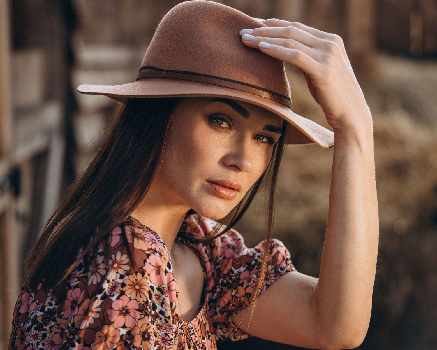 Artistic portrait with brown hat and floral dress in warm sunlight.