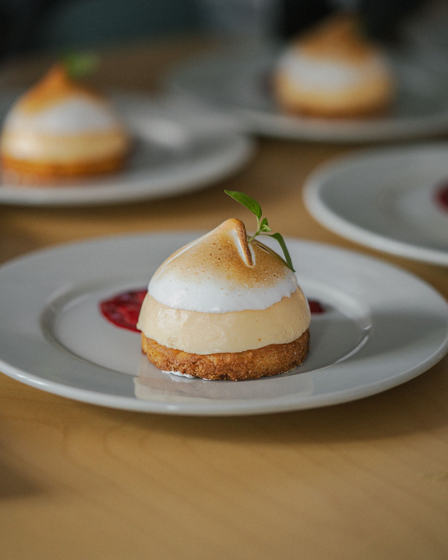 A delicate lemon meringue dessert with a toasted top and fresh herb garnish sits elegantly on a white plate.