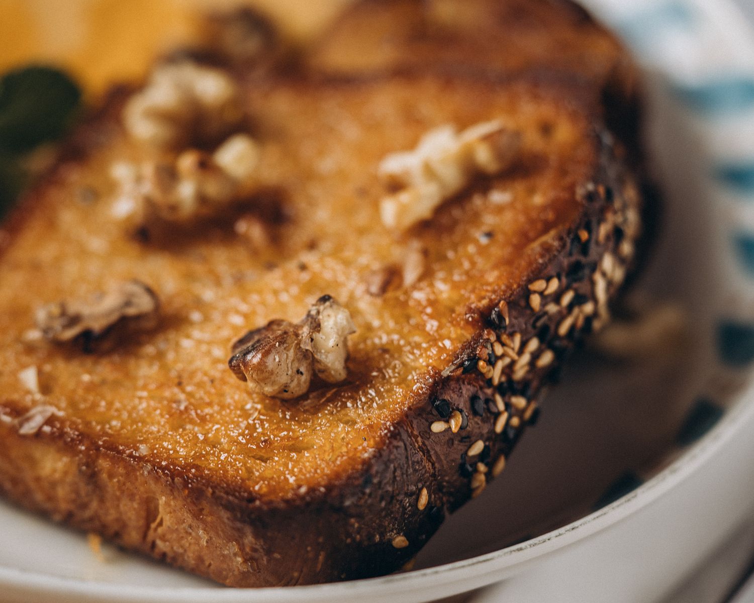 Toasted sesame seed bread topped with walnuts on a white plate in shallow focus.