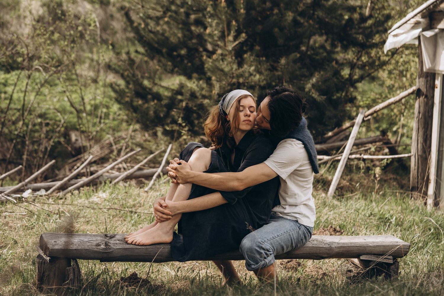 Two people sharing an intimate embrace while sitting on a wooden bench outdoors.