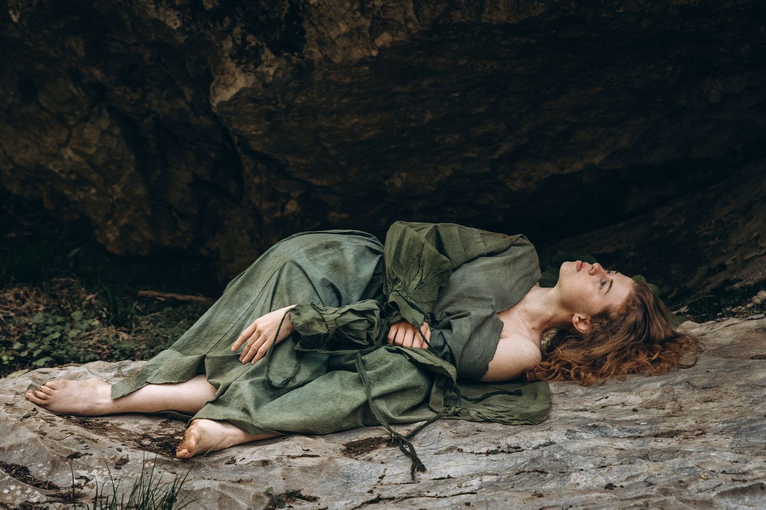 A dreamy portrait of someone reclining on rocks wearing a flowing sage green dress.