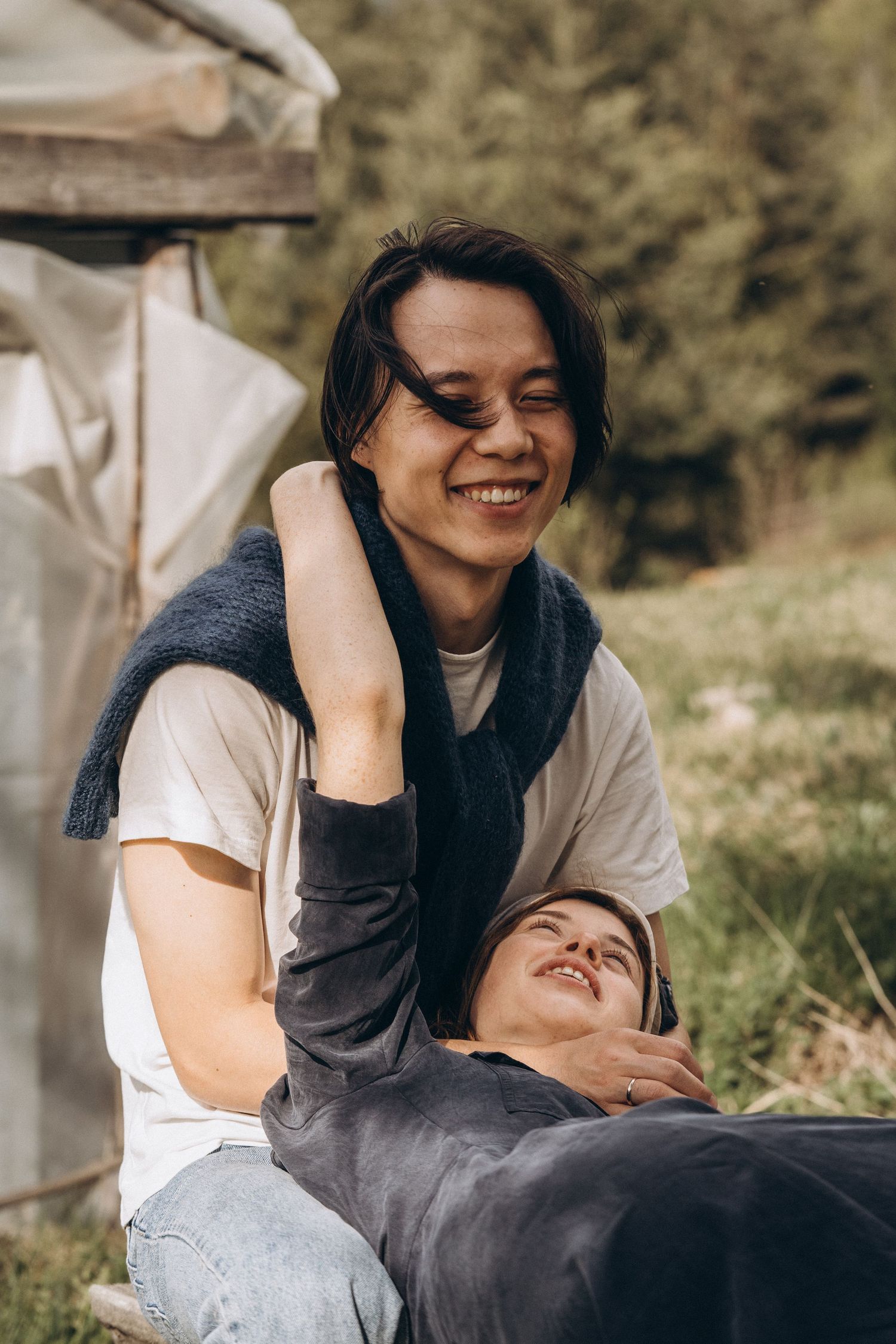 Two people sharing a joyful moment while lying in grass outdoors.