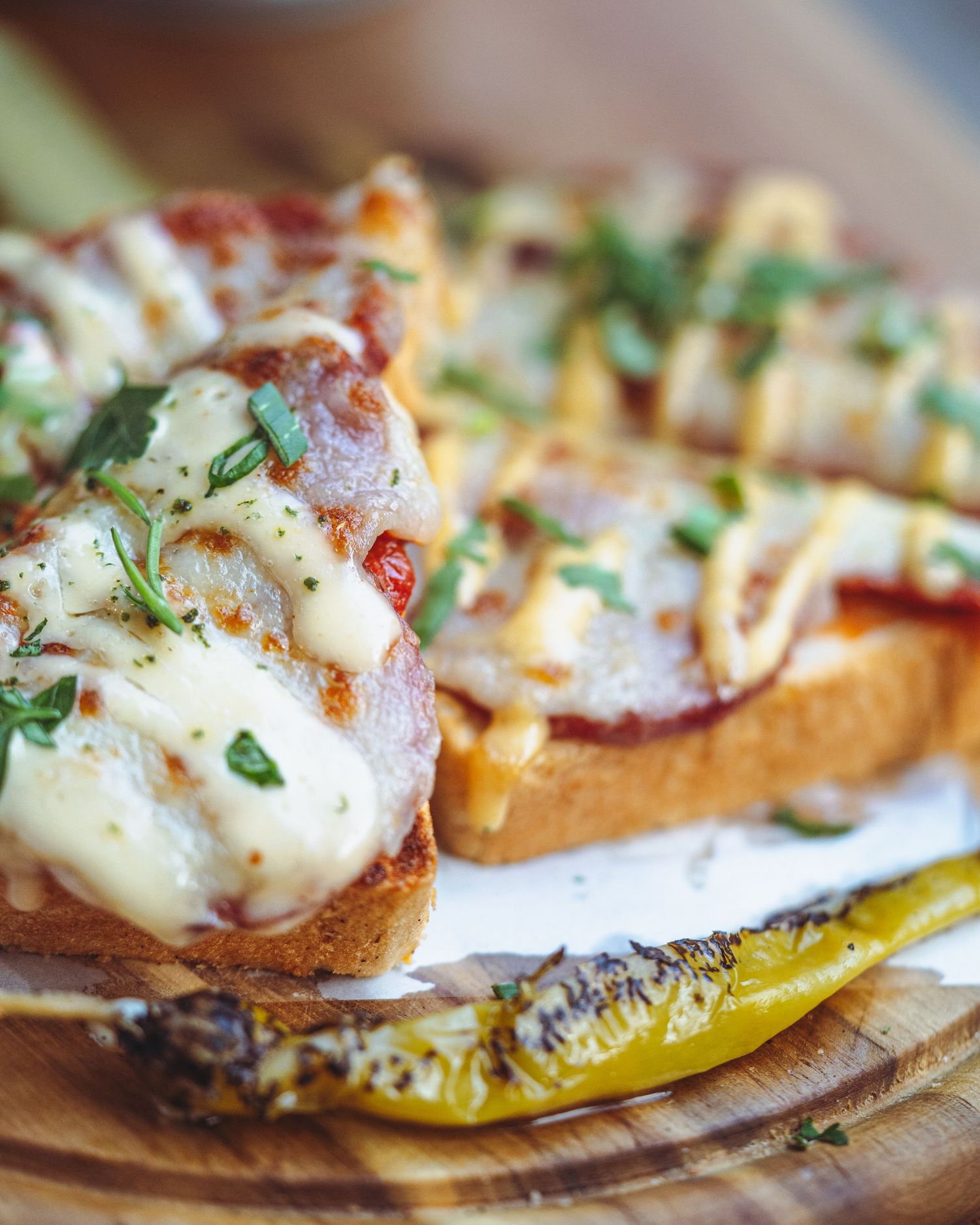 Cheesy garlic bread with melted mozzarella, herbs and roasted peppers on wooden board.