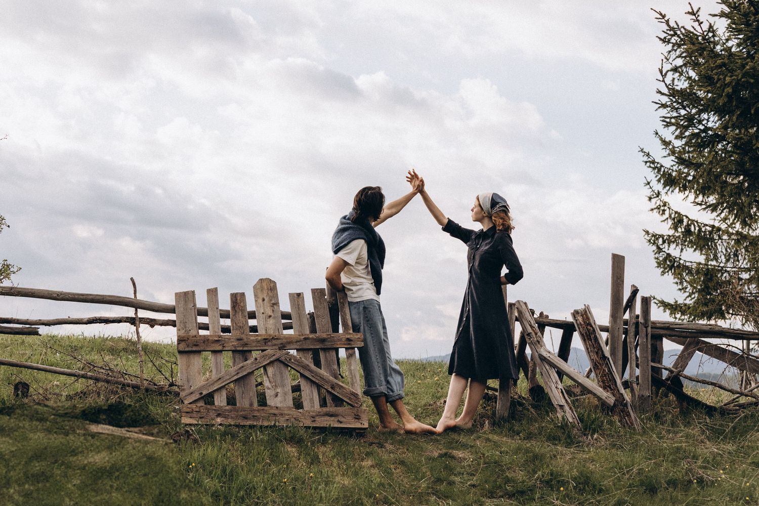 People running and playing together on a grassy hillside with wooden fences.
