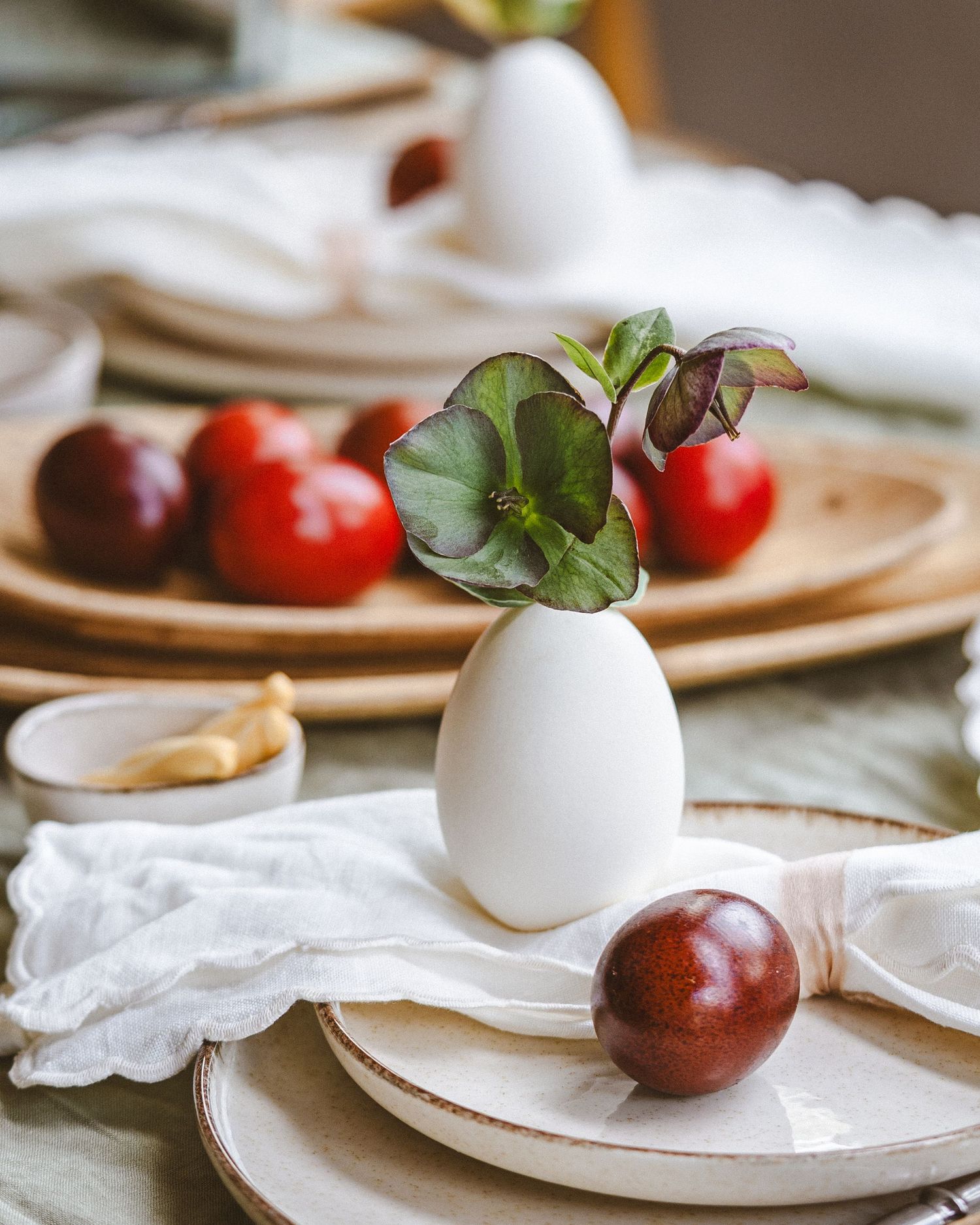 Minimalist place setting with white egg vase, fresh plums, and white linens.
