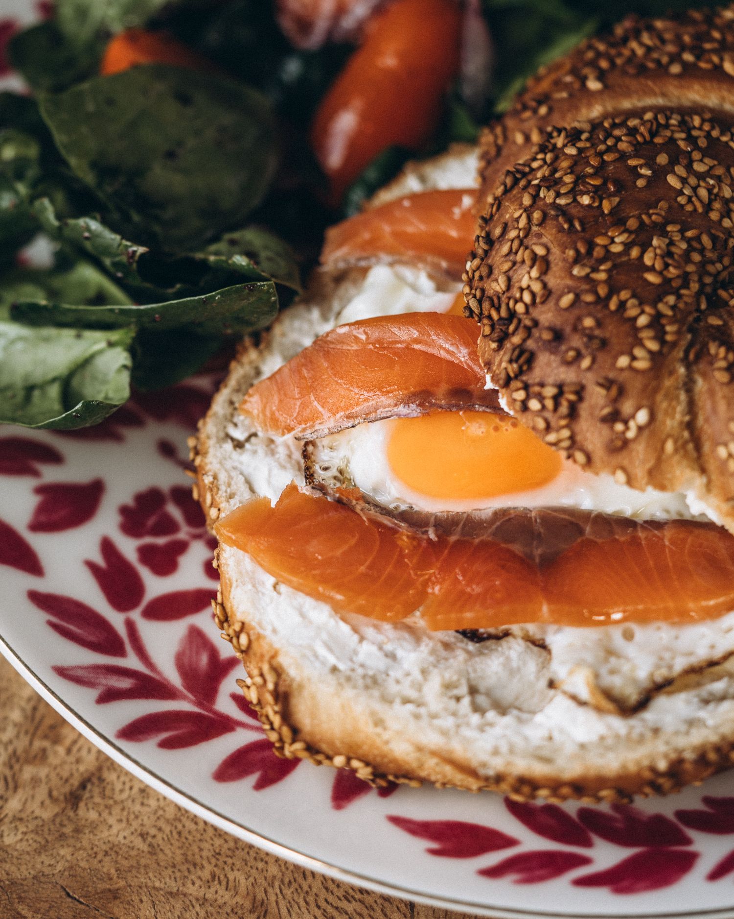 Close-up sequence of a bagel sandwich with smoked salmon, cream cheese and sesame seeds on a decorative plate.