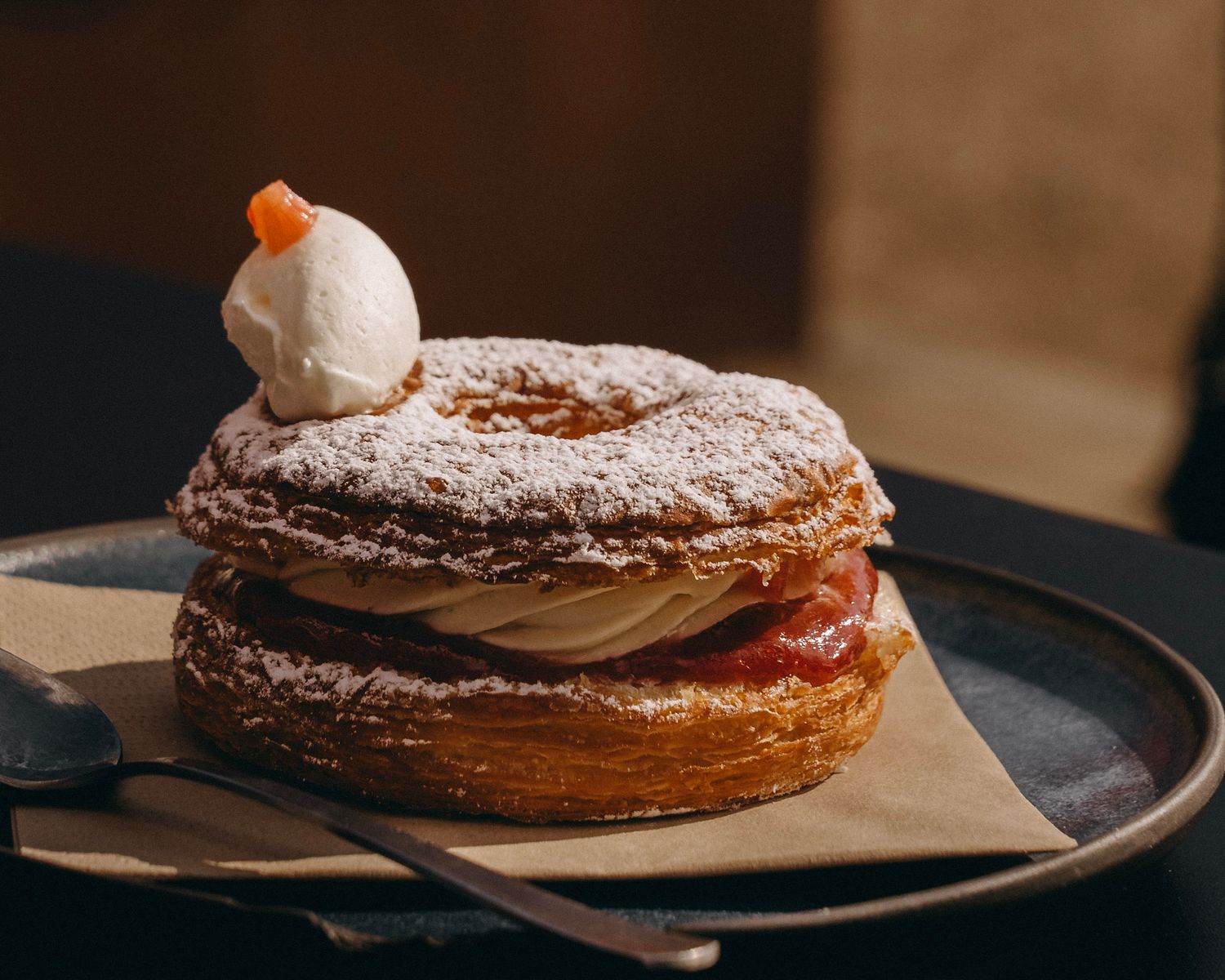 Artisanal pastry with powdered sugar topping served on dark plate with kraft paper.