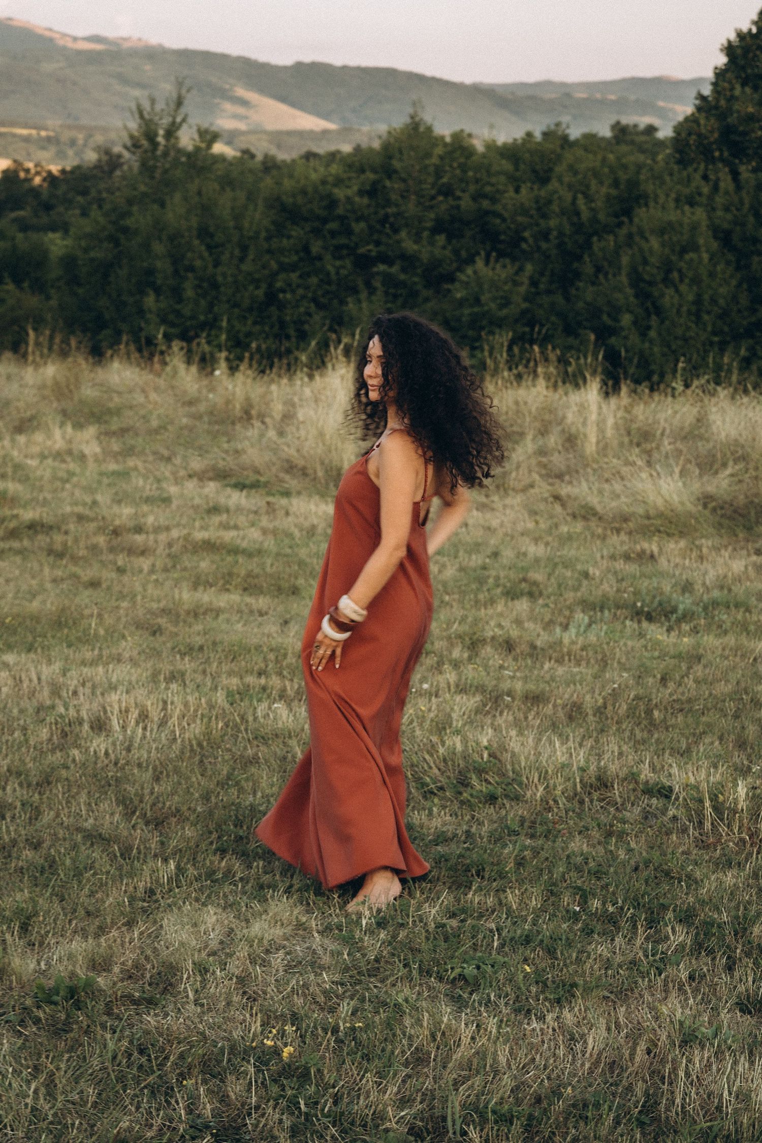 A person in a rust-colored dress standing in a scenic mountain meadow.