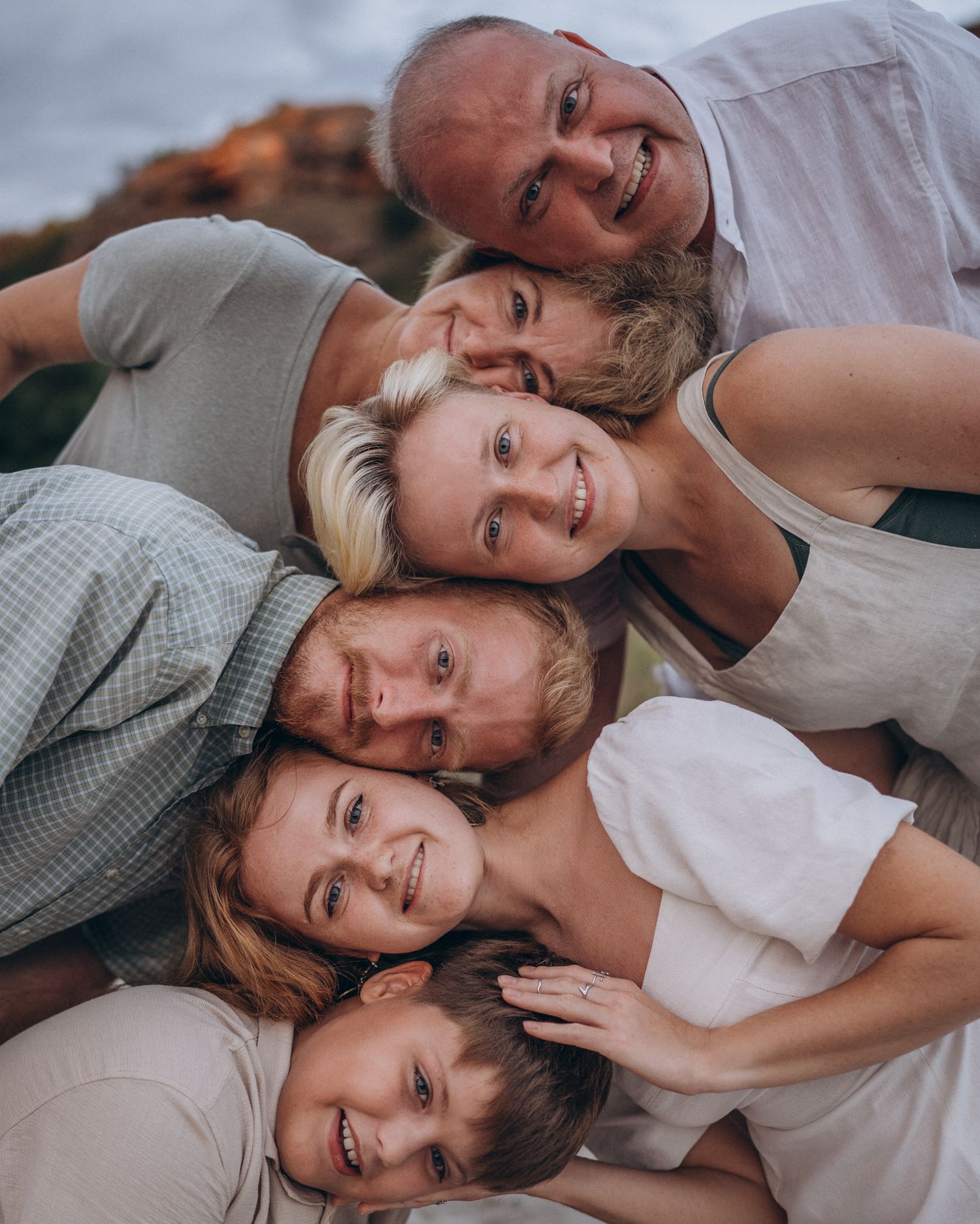 A close-up portrait of a family laying together and smiling at the camera outdoors during golden hour.