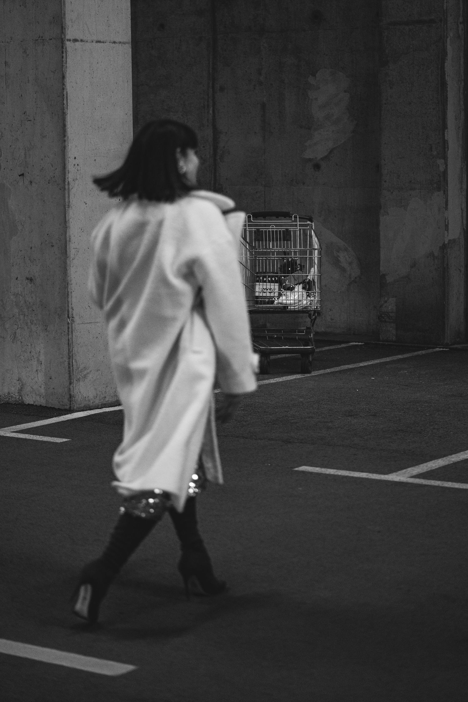 Black and white image of a person in white clothing walking through a dimly lit parking garage.
