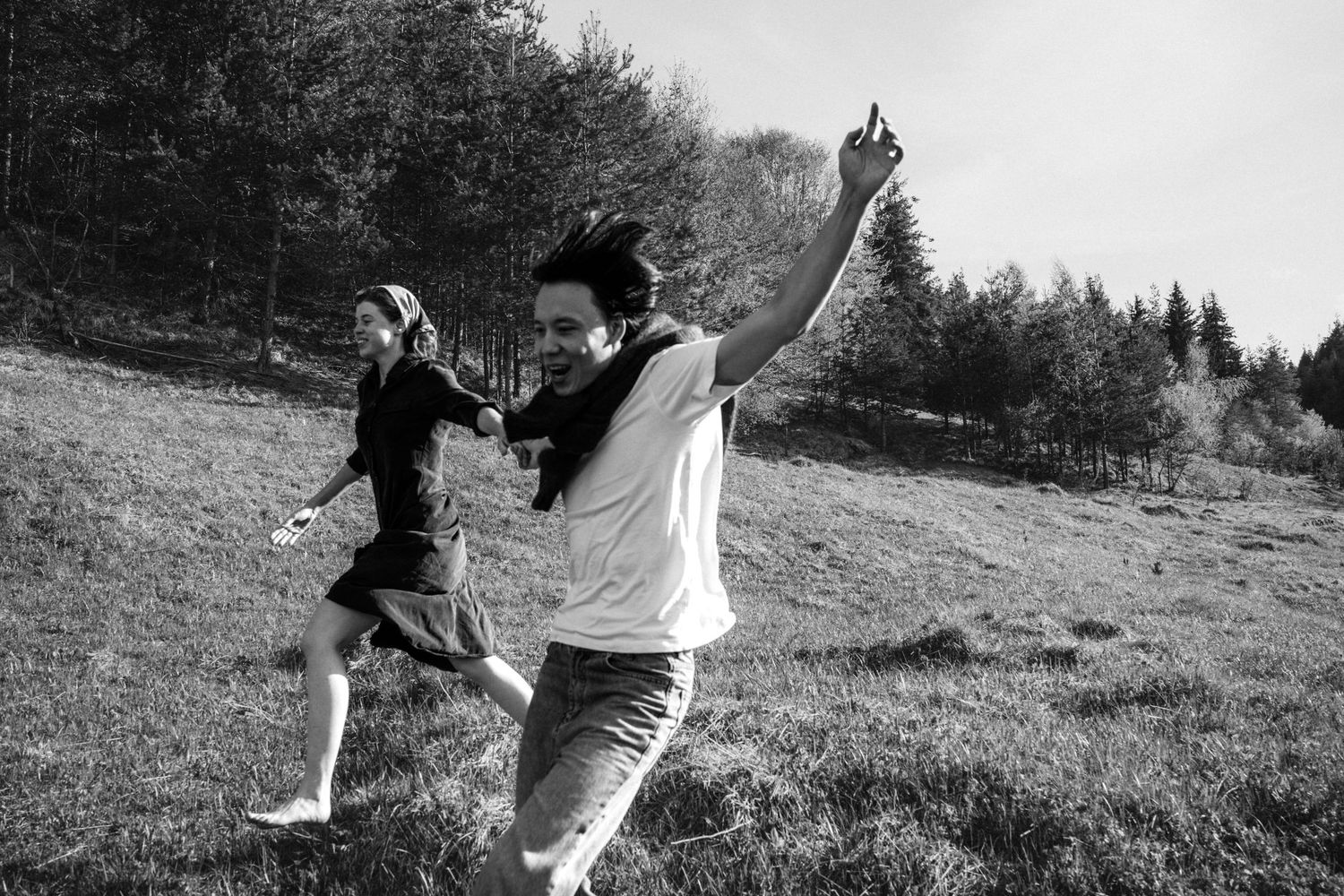 People running and playing together on a grassy hillside in black and white.