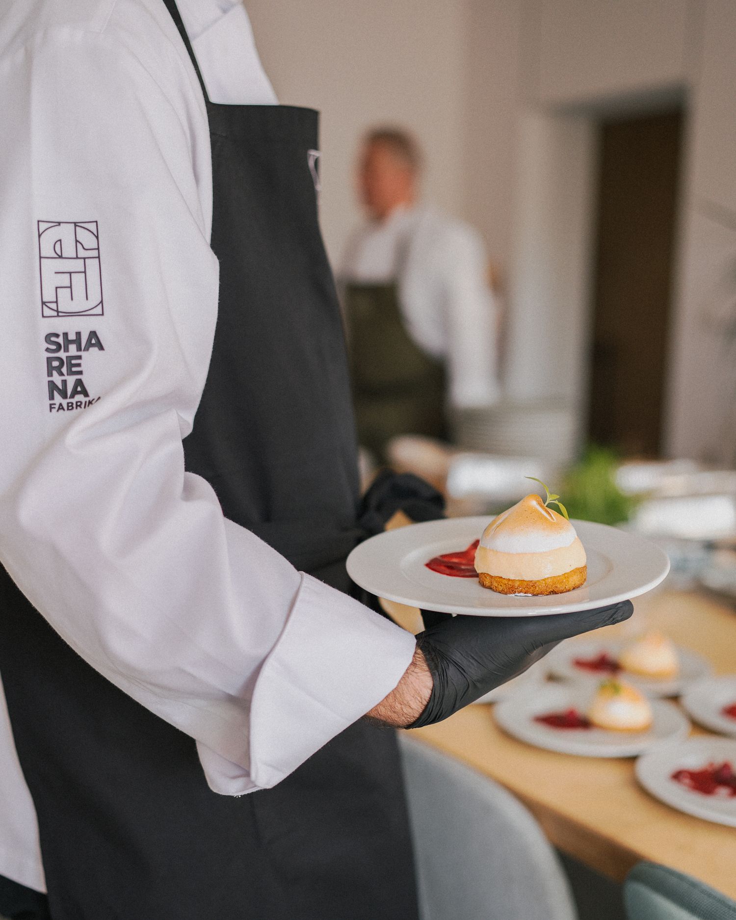 Restaurant server in white shirt and black apron carries plated desserts at an upscale dining establishment.