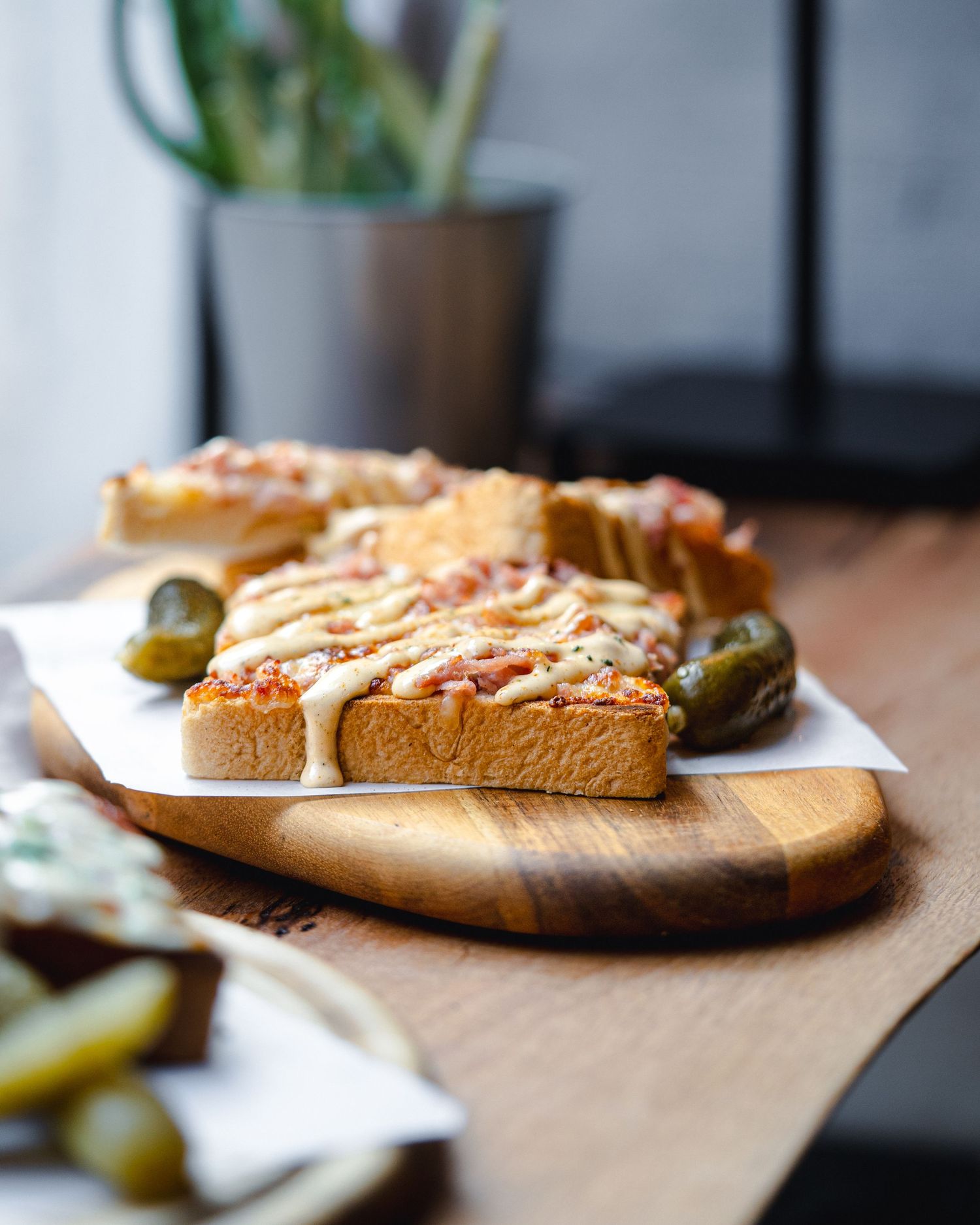 Open-faced sandwich with melted cheese and olives served on a wooden cutting board.