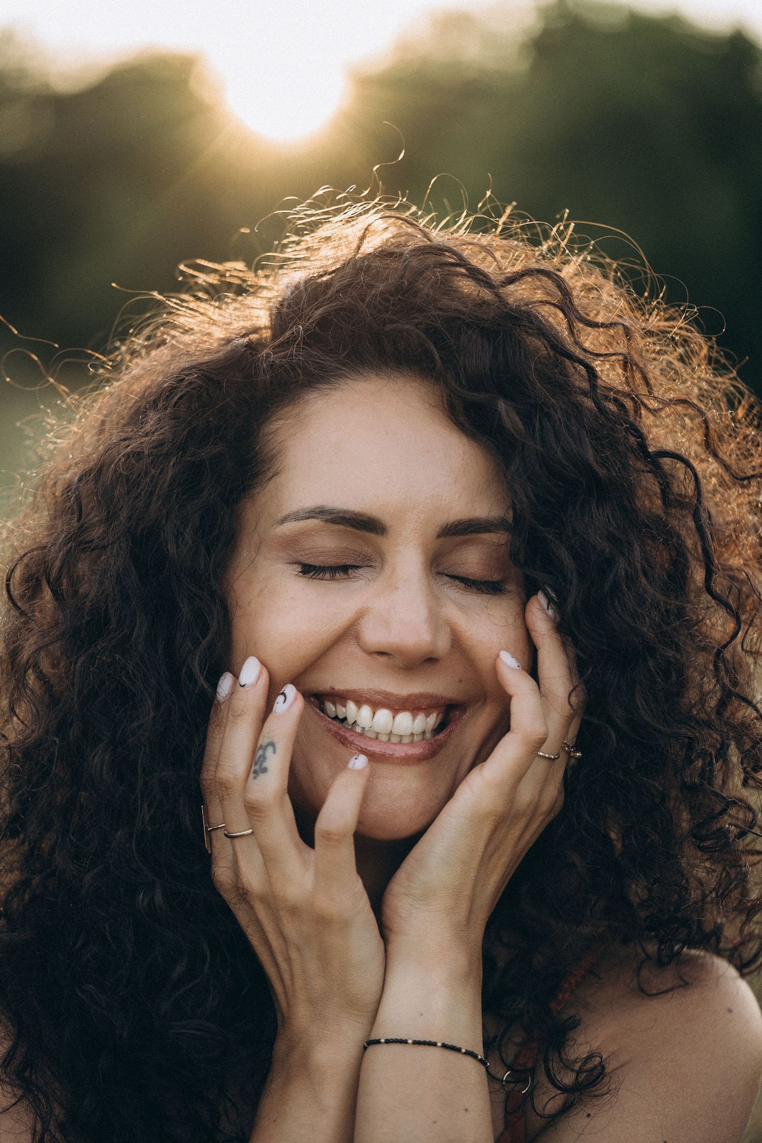 A portrait of curly-haired person with closed eyes smiling in golden sunlight.