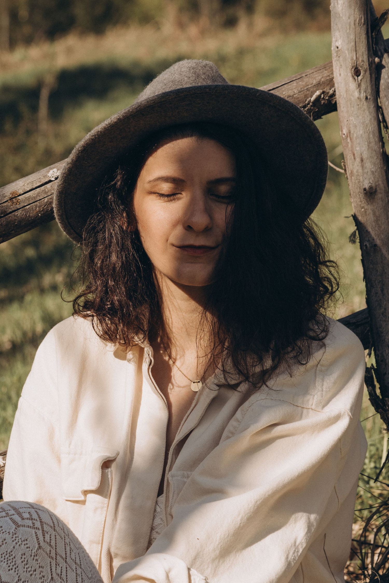 A person in a wide-brimmed hat and white dress relaxes in dappled sunlight outdoors.