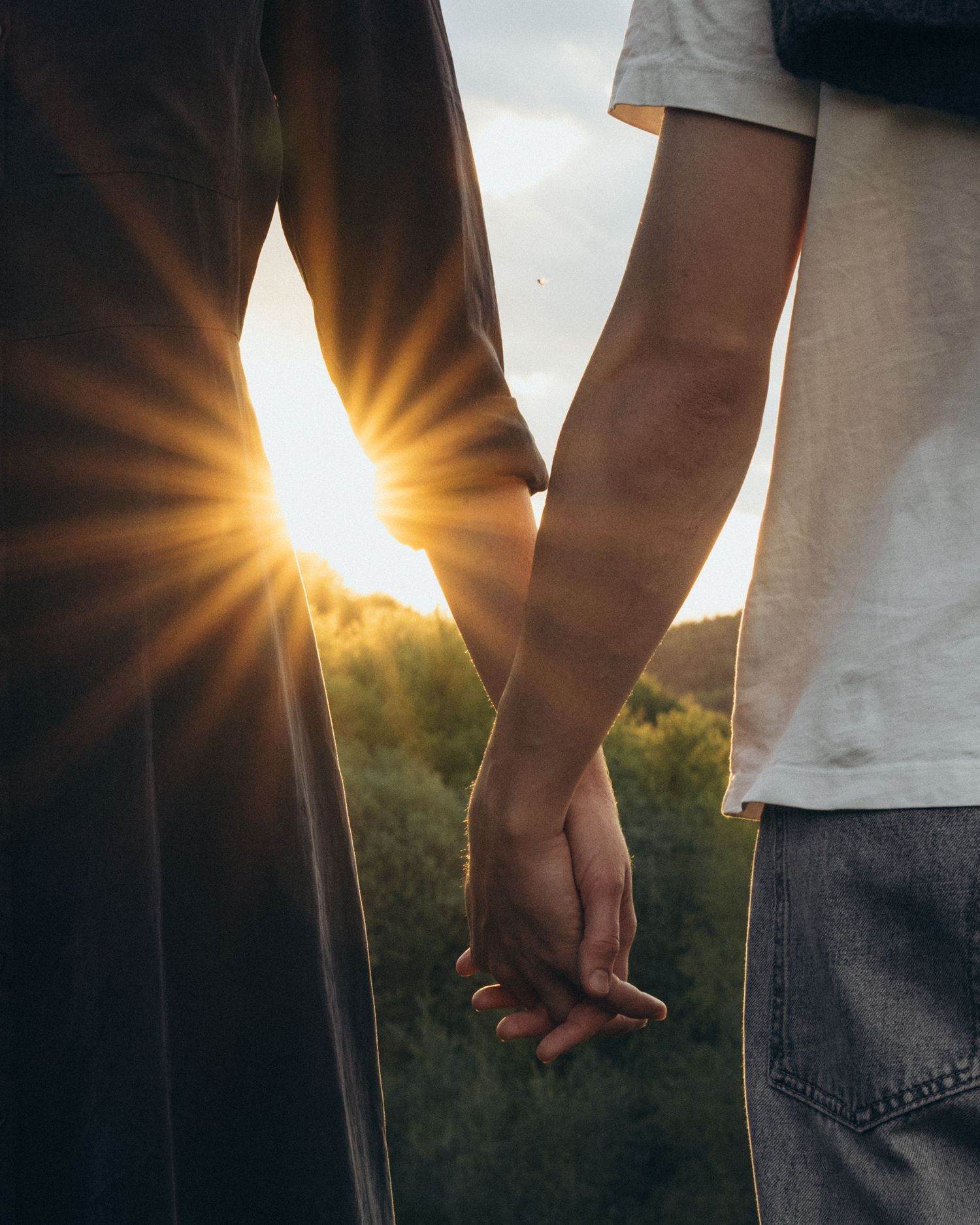 Couple holding hands against golden sunlight in a romantic outdoor setting.
