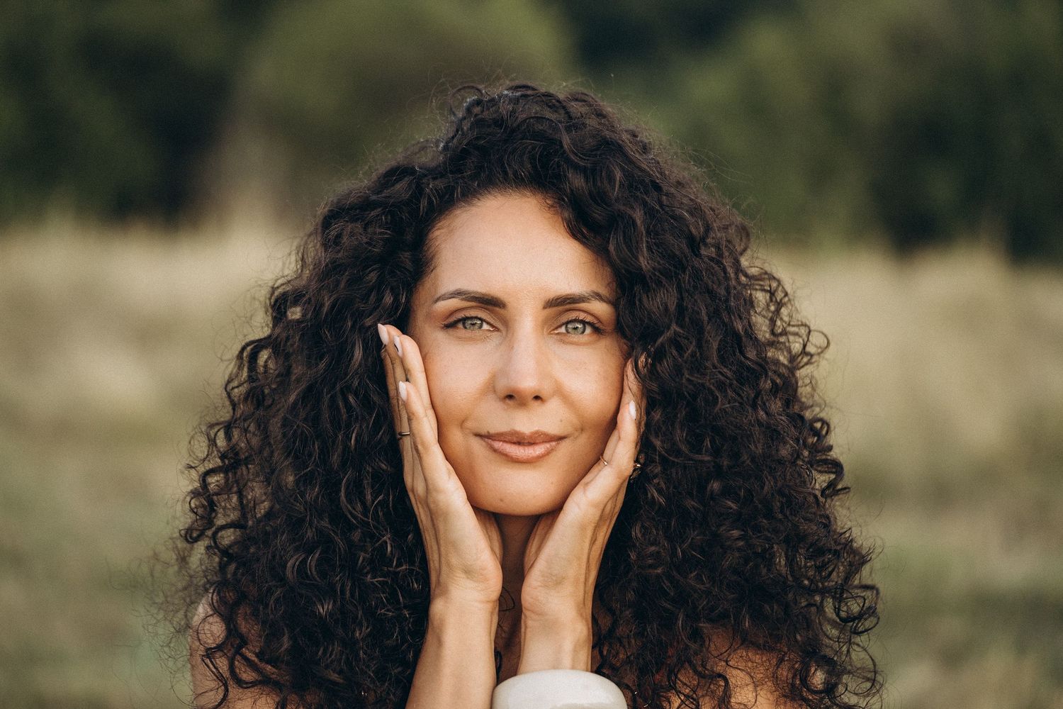 A portrait showing hands gently touching cheeks in warm sunlight.