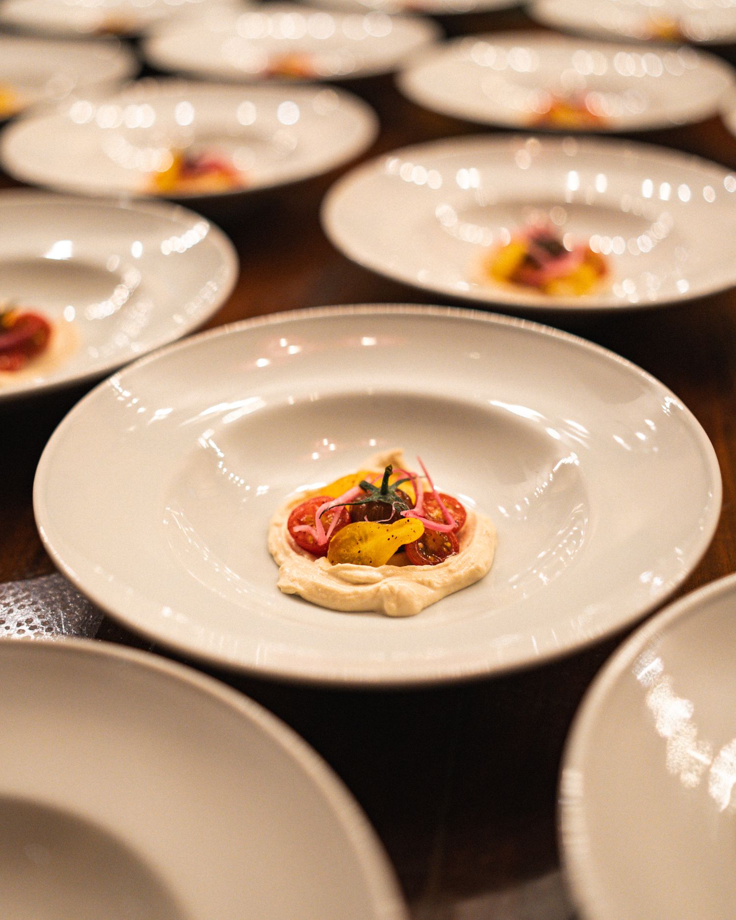 Multiple white plates of elegantly plated dishes lined up in a restaurant kitchen preparation area.