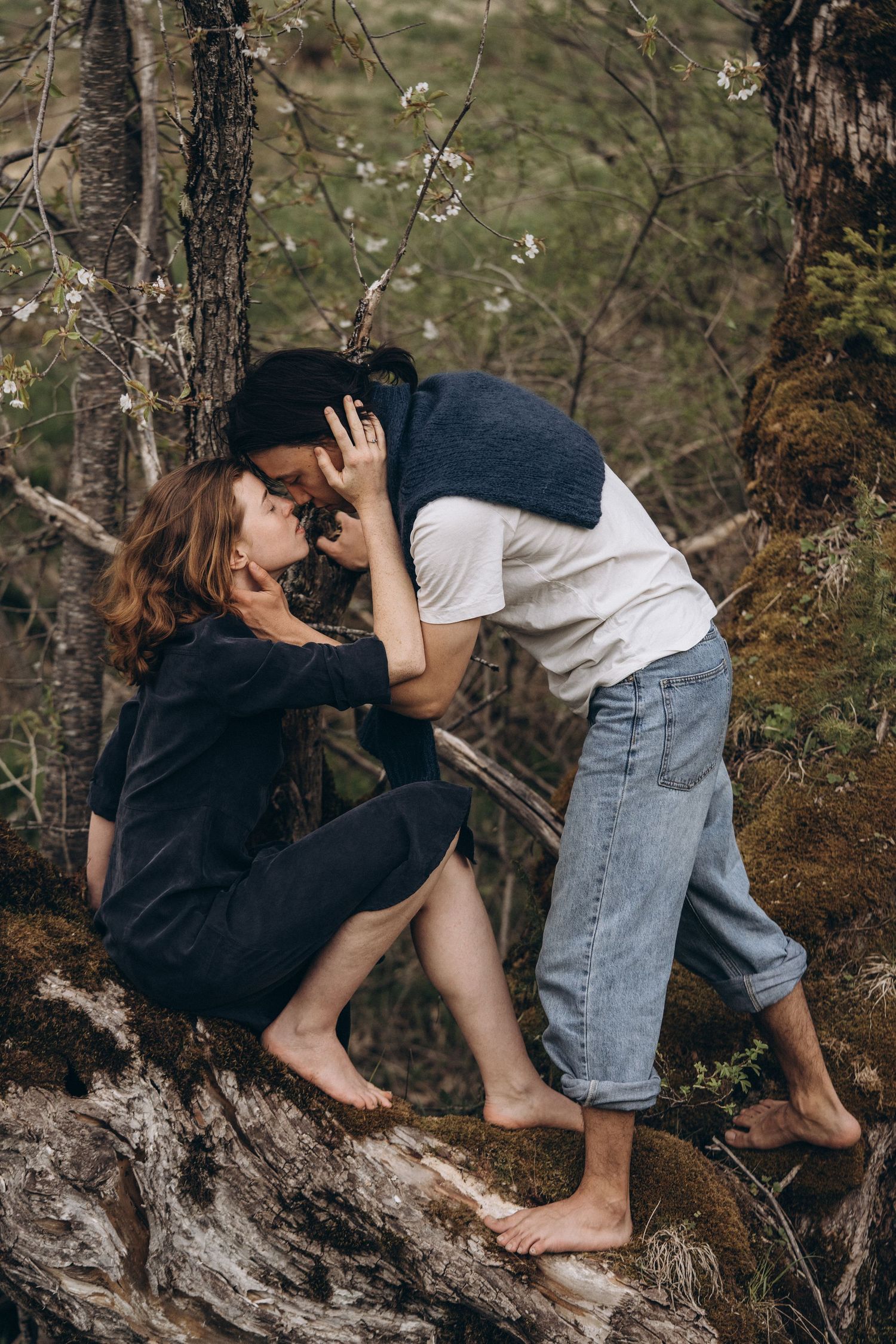 Two people share playful moments while barefoot on a fallen tree trunk.