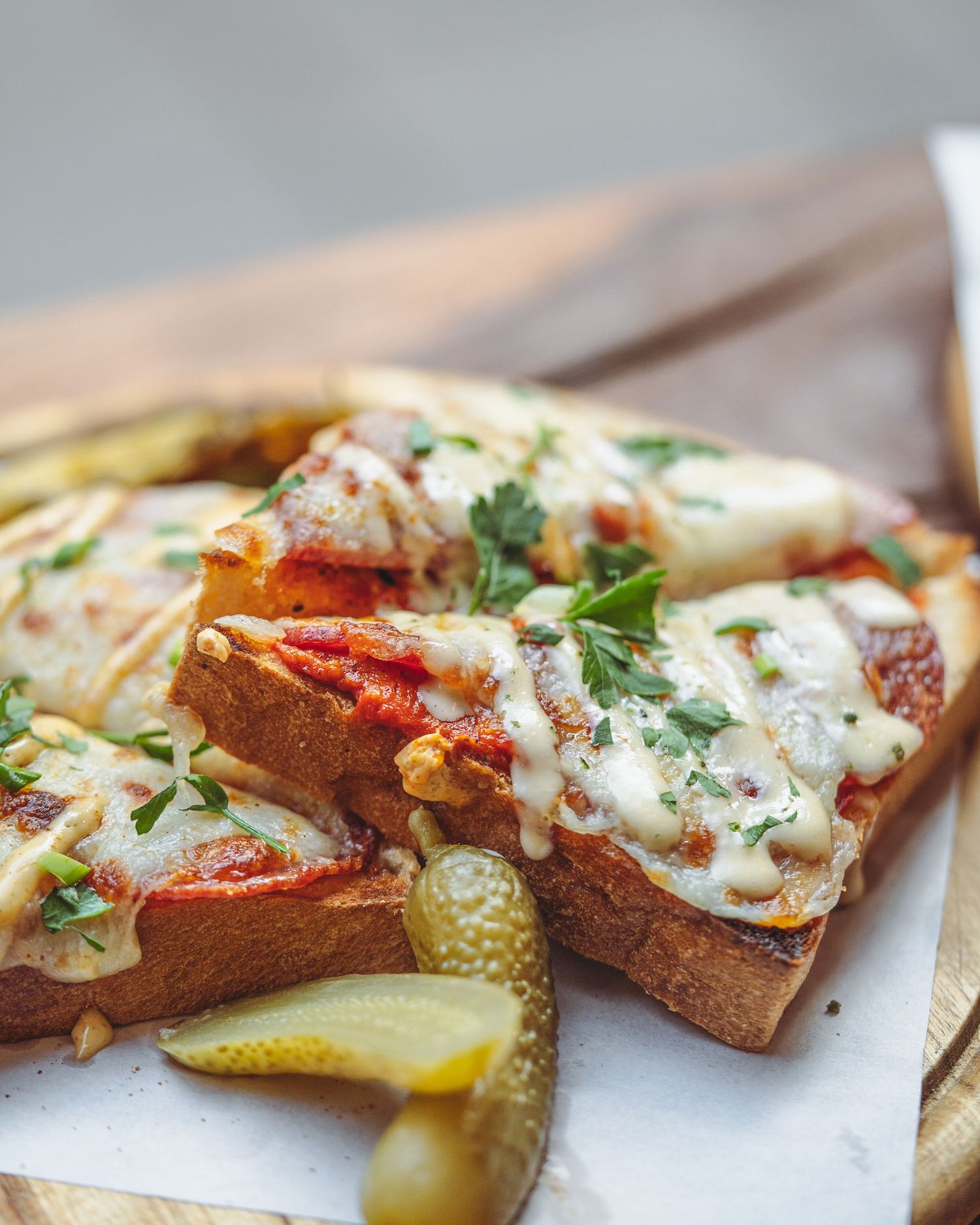 Gourmet open-faced sandwich with melted cheese, herbs, and pickles on toasted bread.