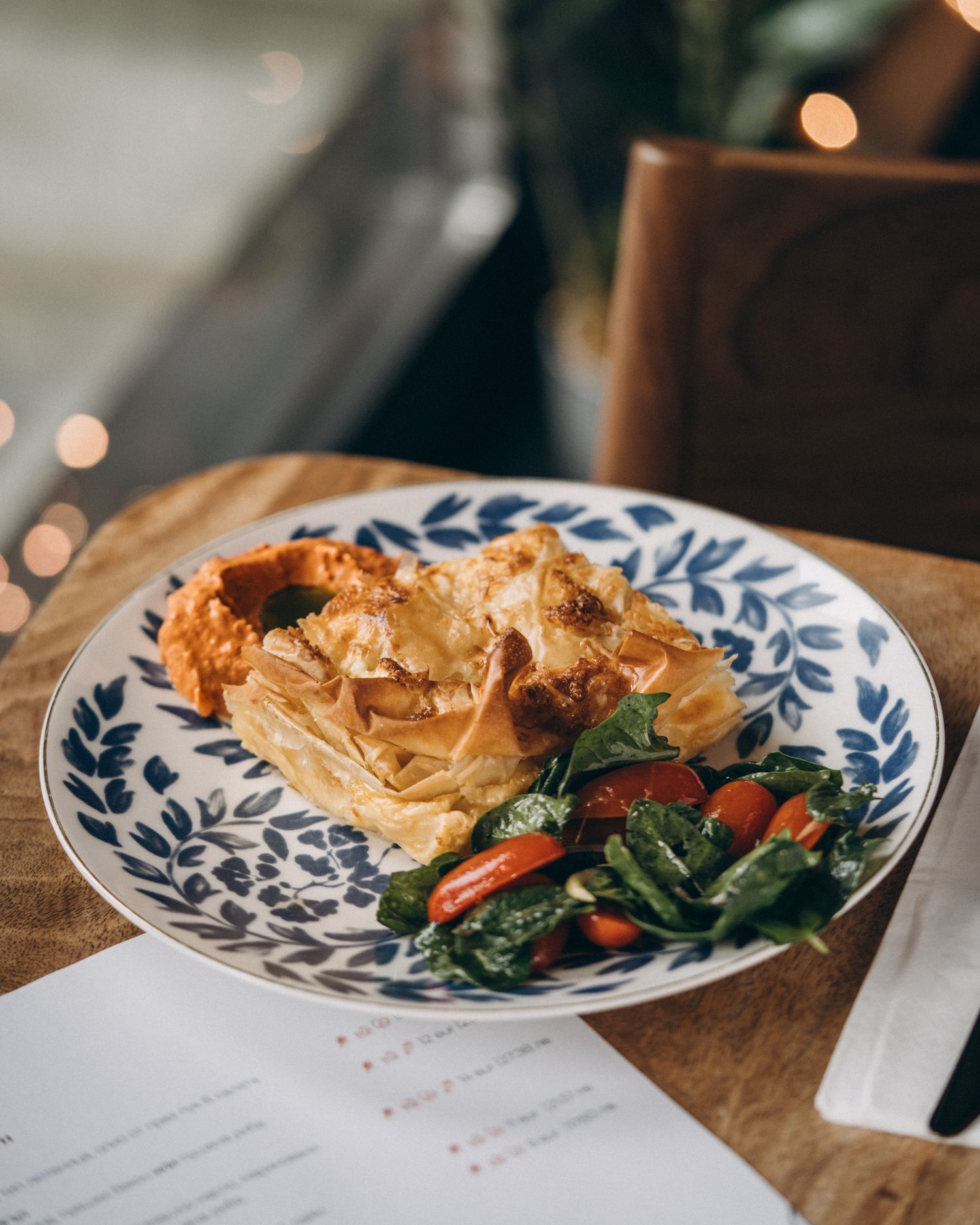 A plate with flaky pastry and sautéed vegetables served on a blue and white patterned dish in warm lighting.