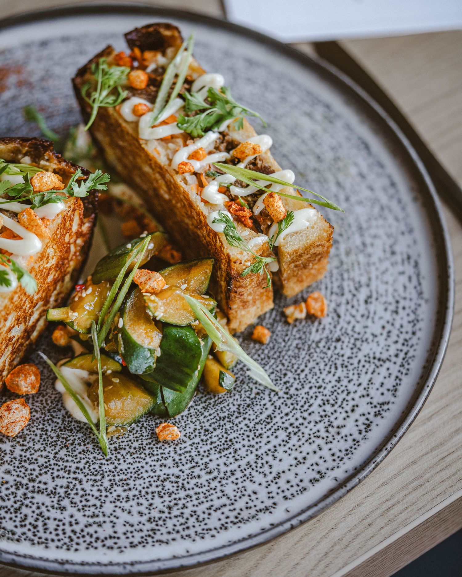 Beautifully presented appetizers with greens and sauce on a speckled gray plate.