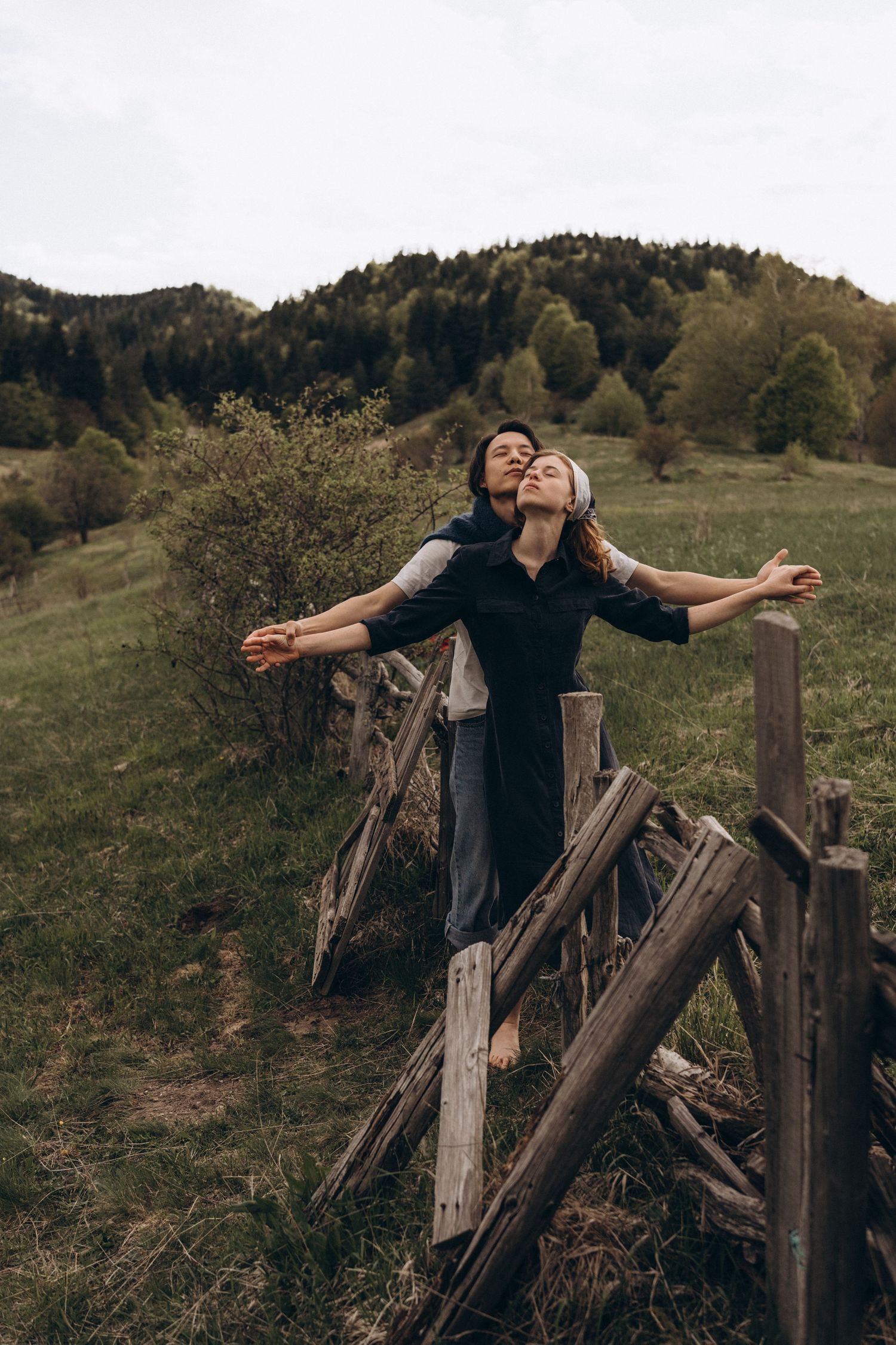 Two people sharing a joyful moment while leaning on an old wooden fence in a rural setting.