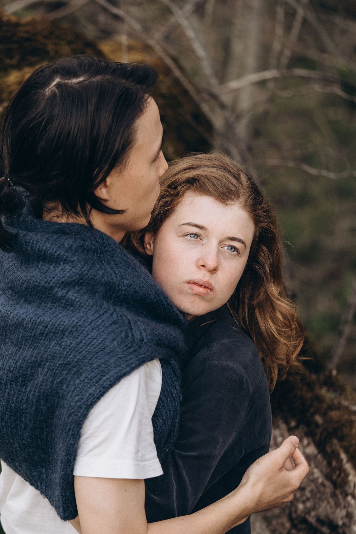 A tender embrace captured in soft natural lighting against a blurred forest backdrop.
