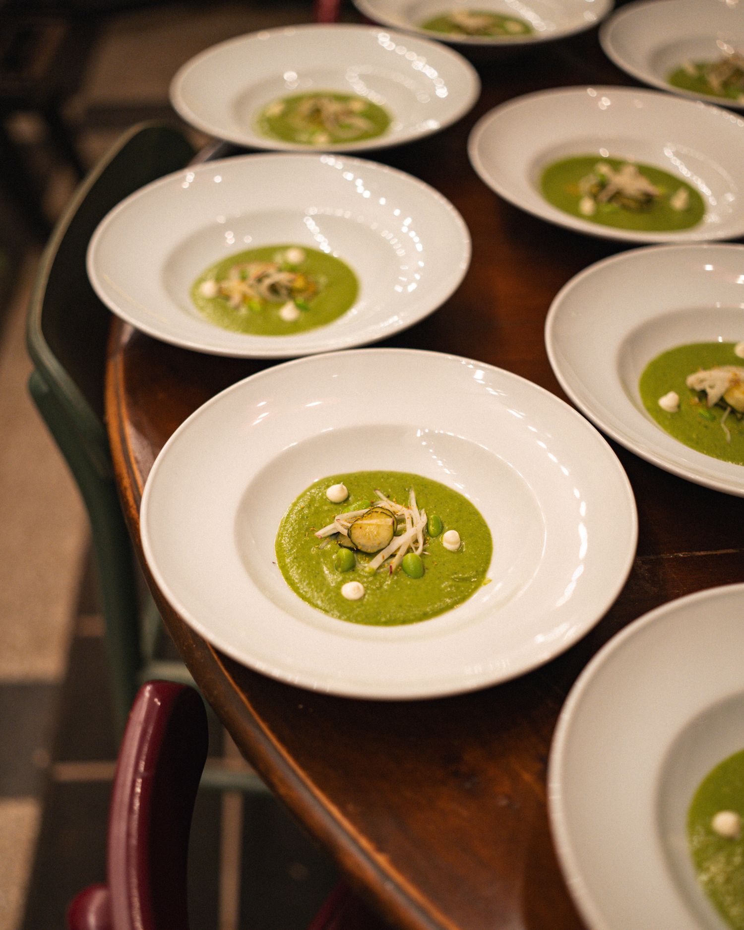 Multiple white bowls of vibrant green soup garnished with toppings arranged on a dark wooden surface.