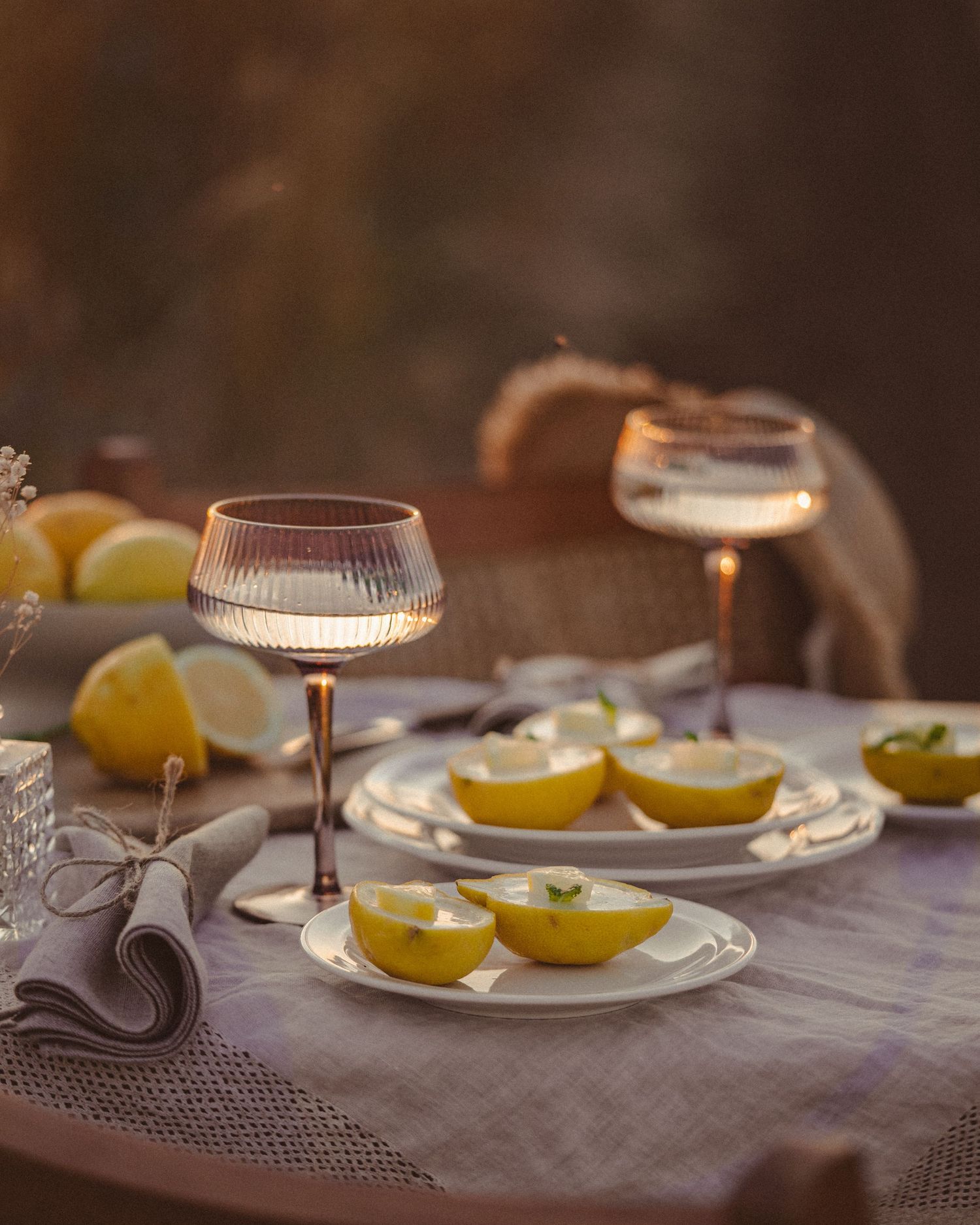 Elegant table setting with crystal wine glasses and fresh lemon slices on white plates in moody lighting.
