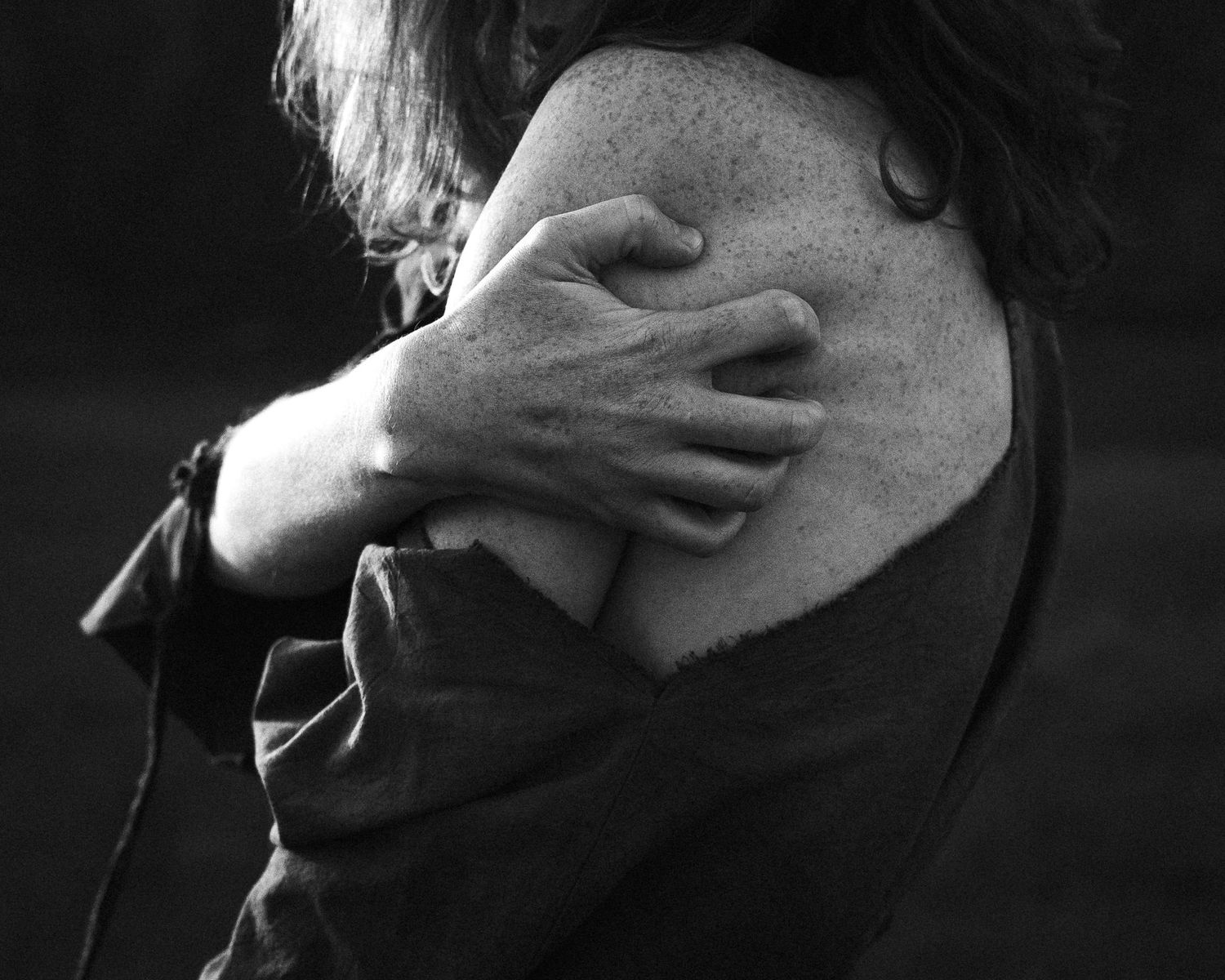Dramatic black and white close-up of hands covering face in shadow.