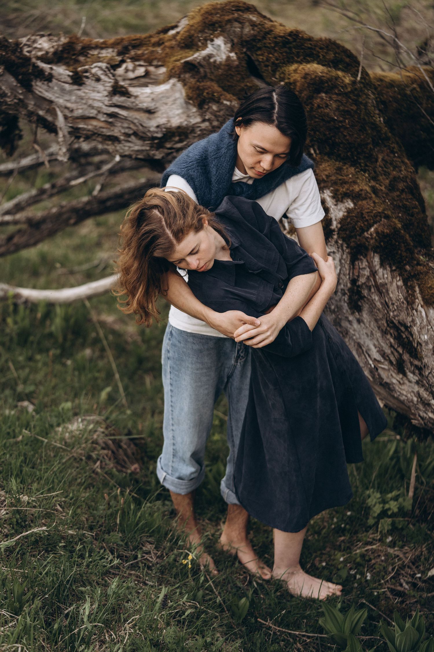 Two people sharing an intimate moment outdoors near a tree trunk in a natural setting.
