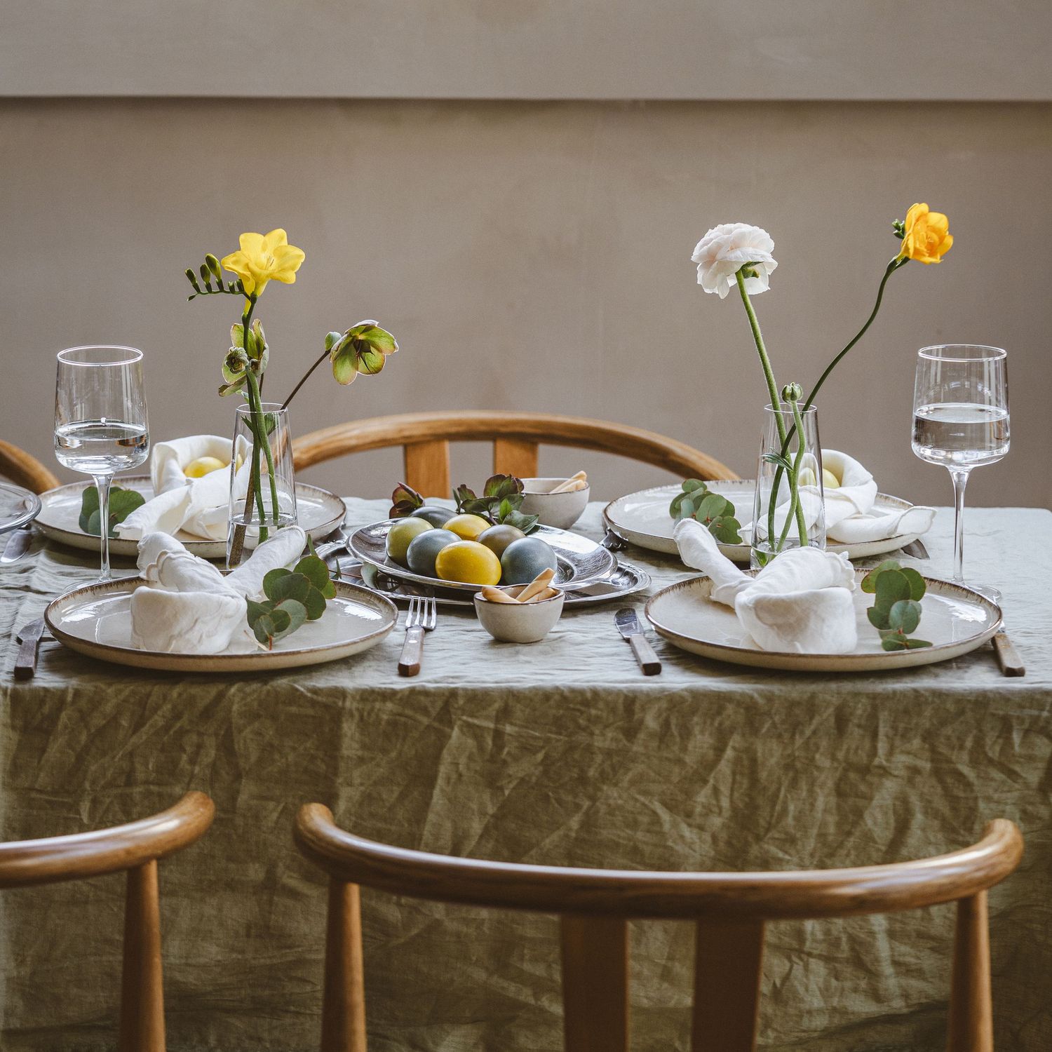 Minimalist dining table set with yellow flowers, water glasses, and sage green linens.
