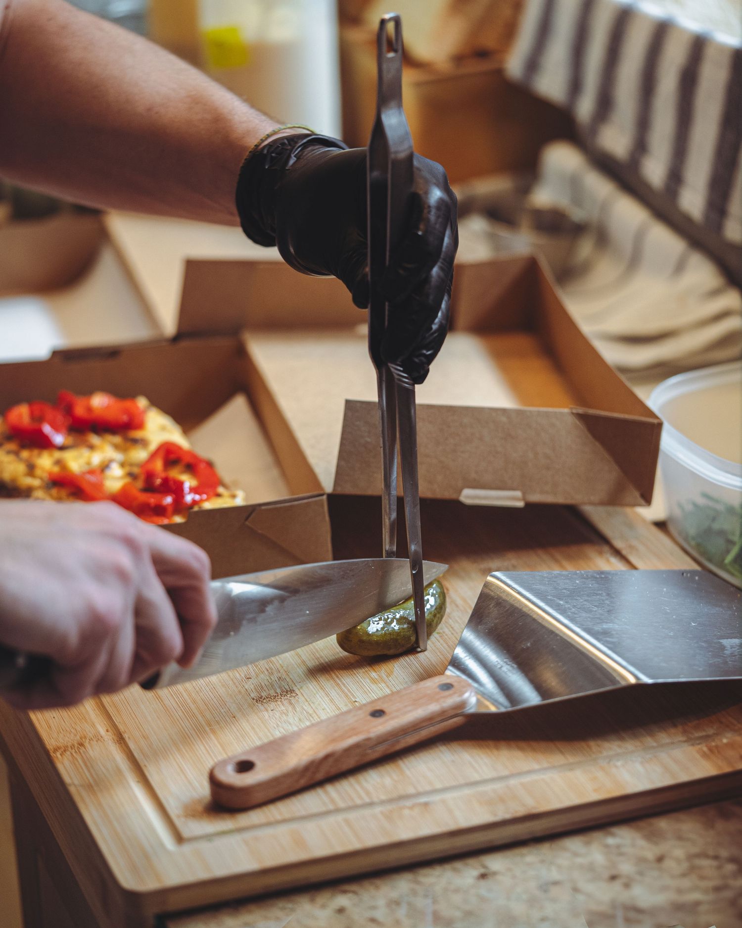 Hands in black gloves cutting food on a wooden cutting board next to a pizza box.