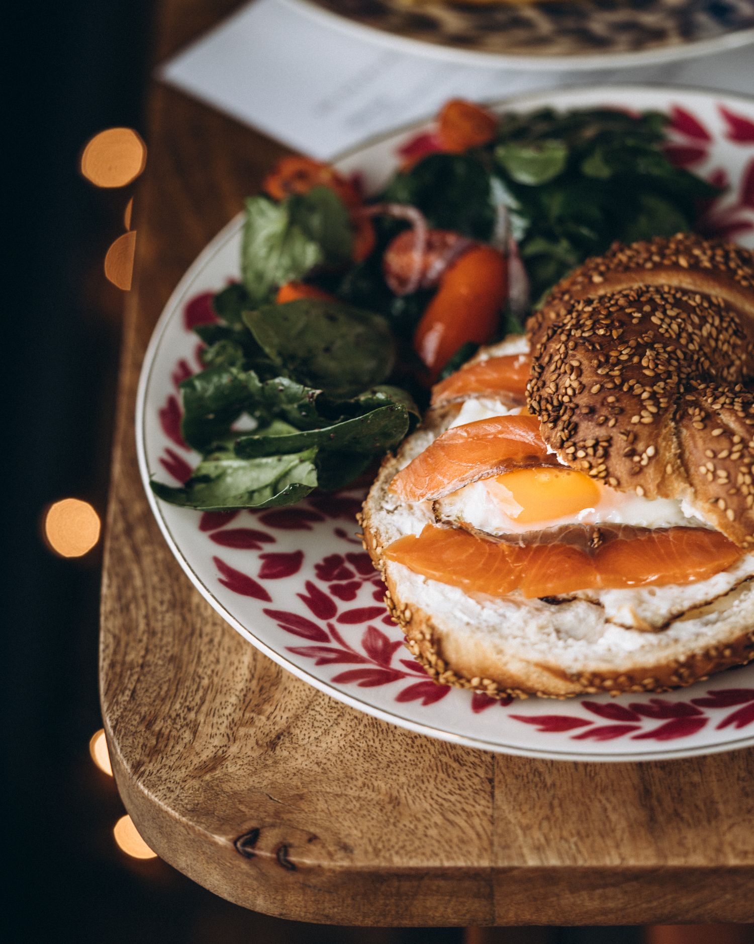 A sesame seed bagel topped with cream cheese, smoked salmon, and a perfectly poached egg on a decorative plate.