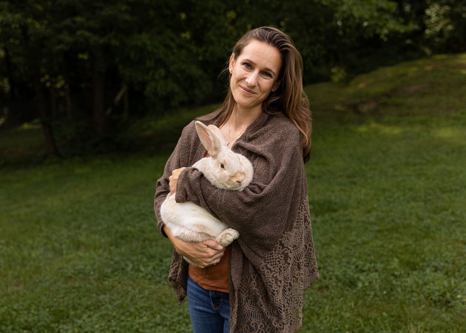 Woman smiling while holding a Crème d’Argent rabbit in a green grassy field.