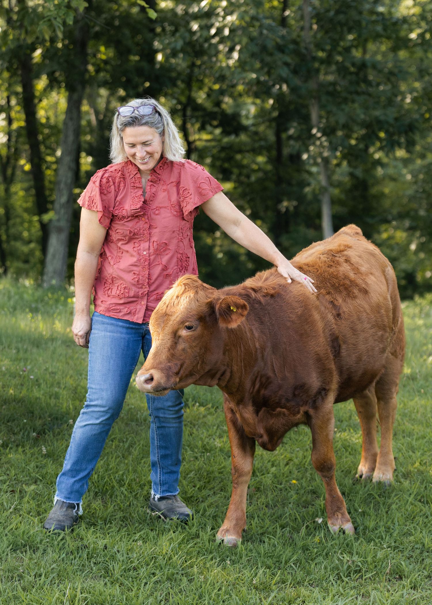 Woman in red shirt petting a Dexter calf in a green pasture.