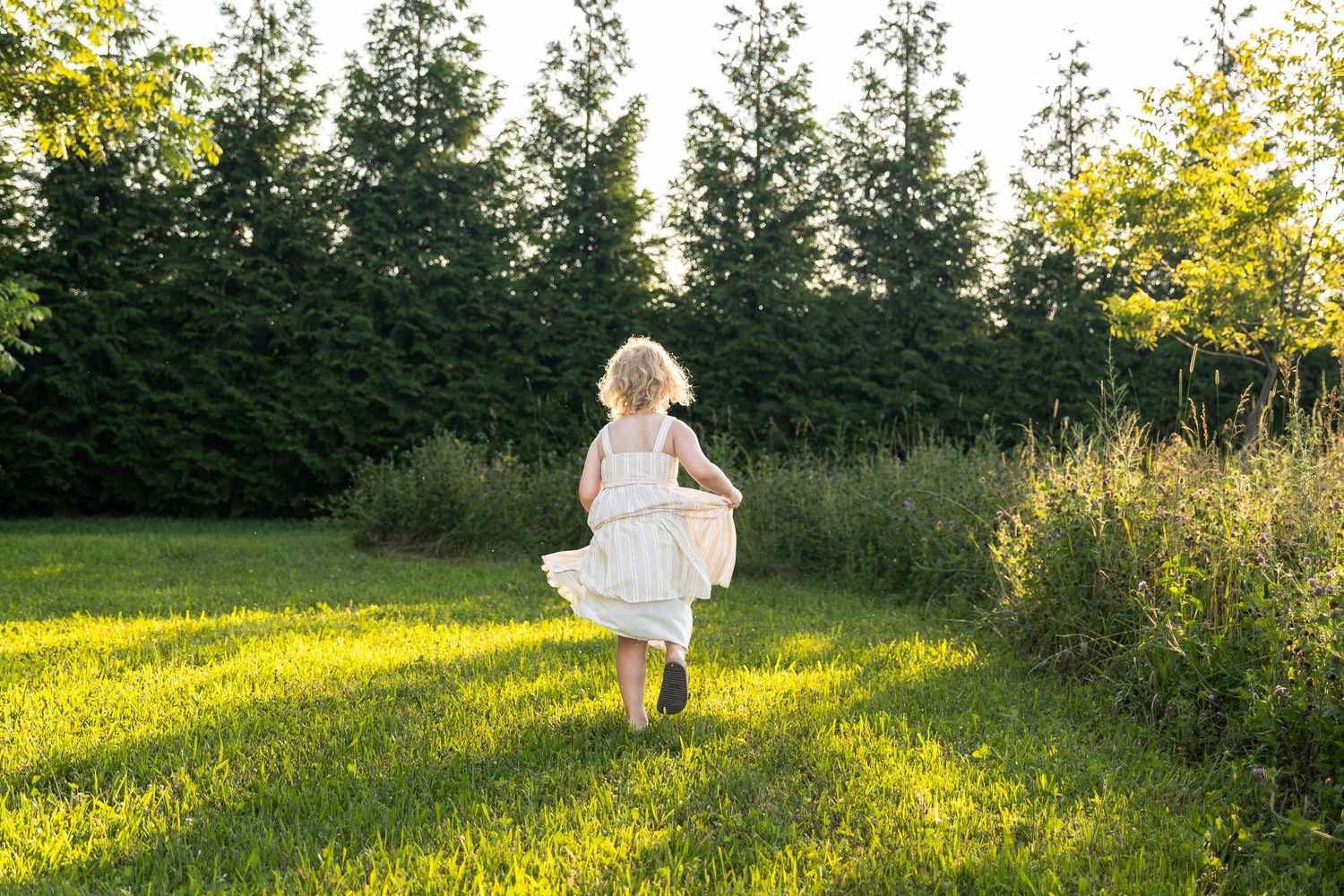 Young girl in white dress twirling in sunny green meadow.