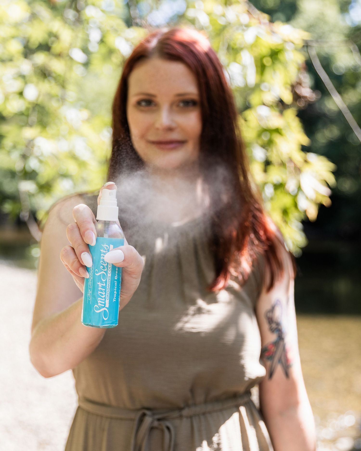 Red-haired woman spraying blue bottle of pet grooming product toward camera outdoors.
