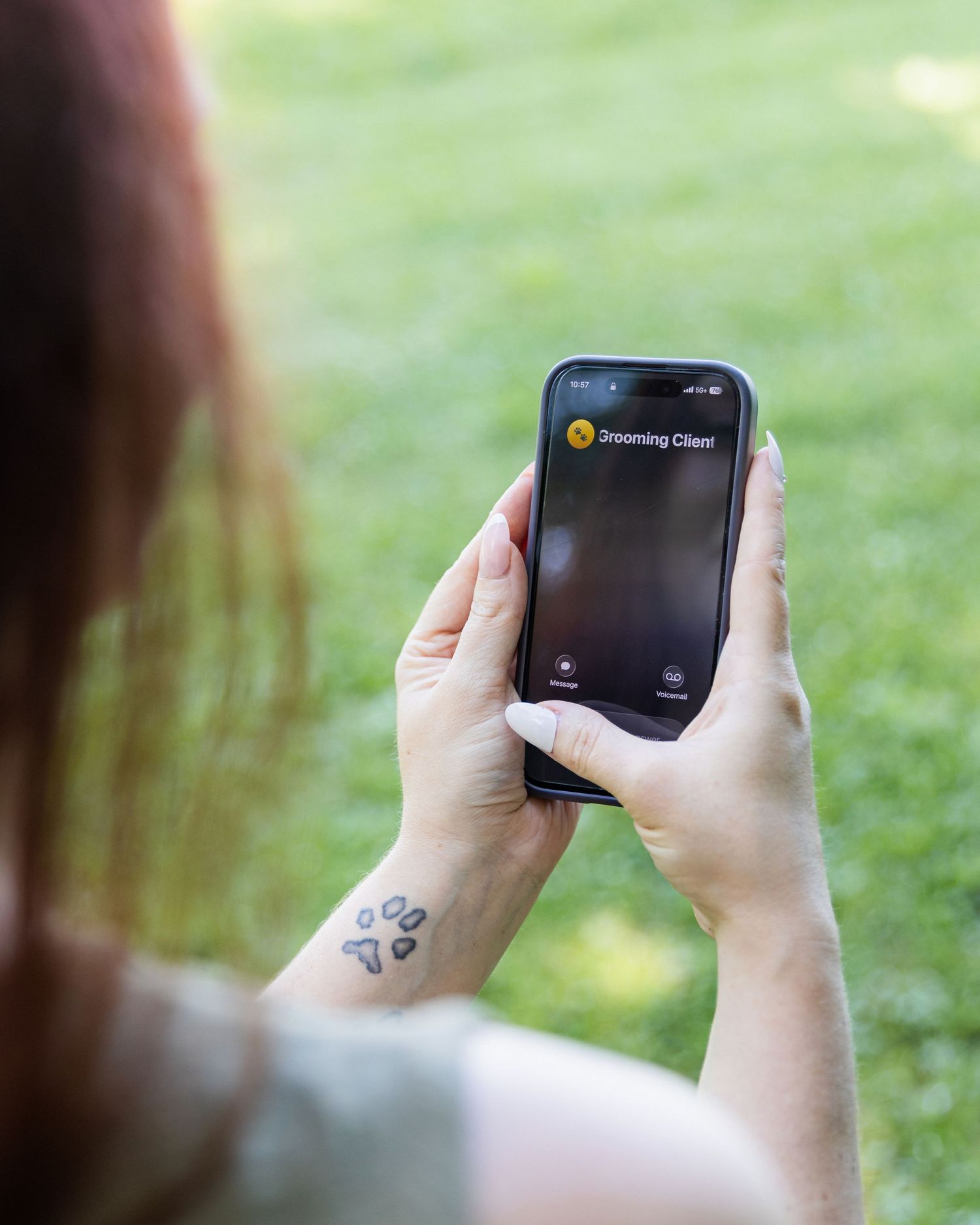 Woman holding smartphone displaying grooming client call screen outdoors.