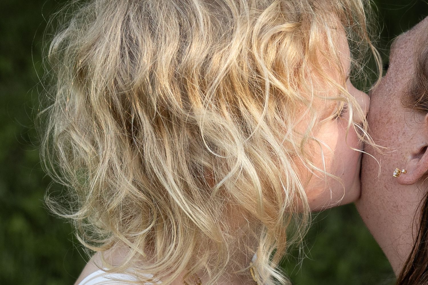 Close-up of curly blonde child giving a kiss on cheek outdoors.
