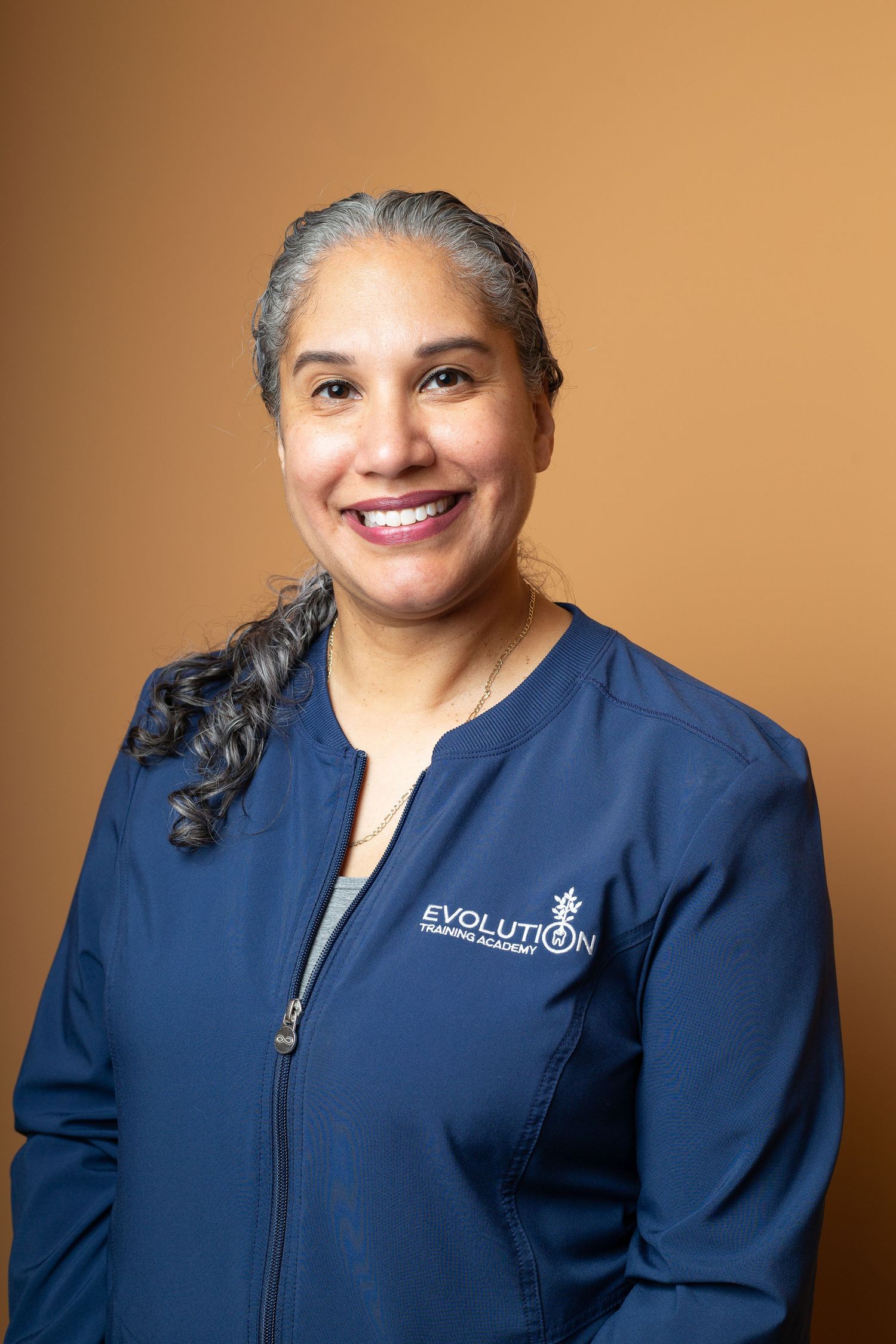 Healthcare professional in navy blue scrubs smiles warmly against a warm brown background in a series of portraits.