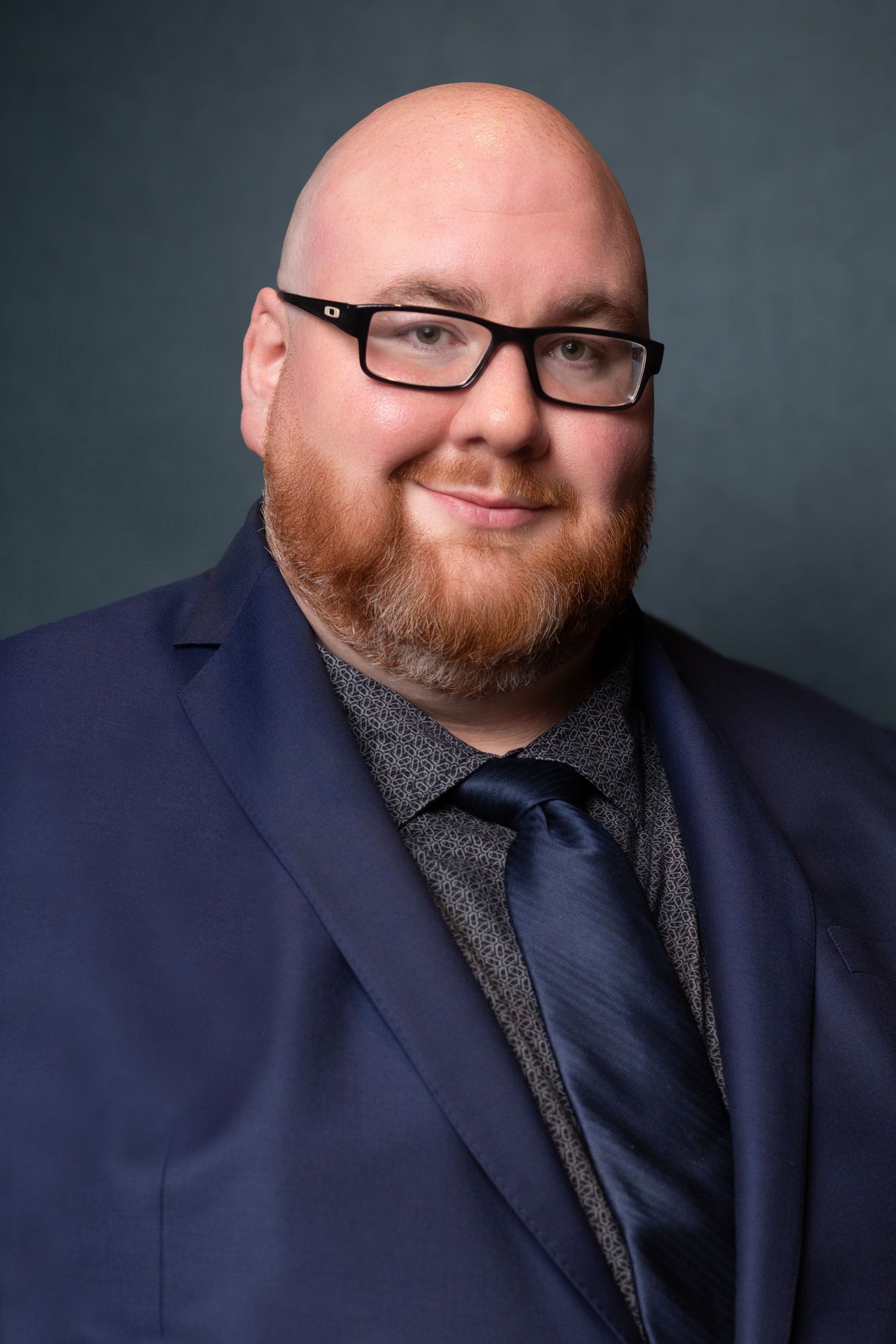Professional headshots of person in navy suit and patterned tie against dark backdrop.