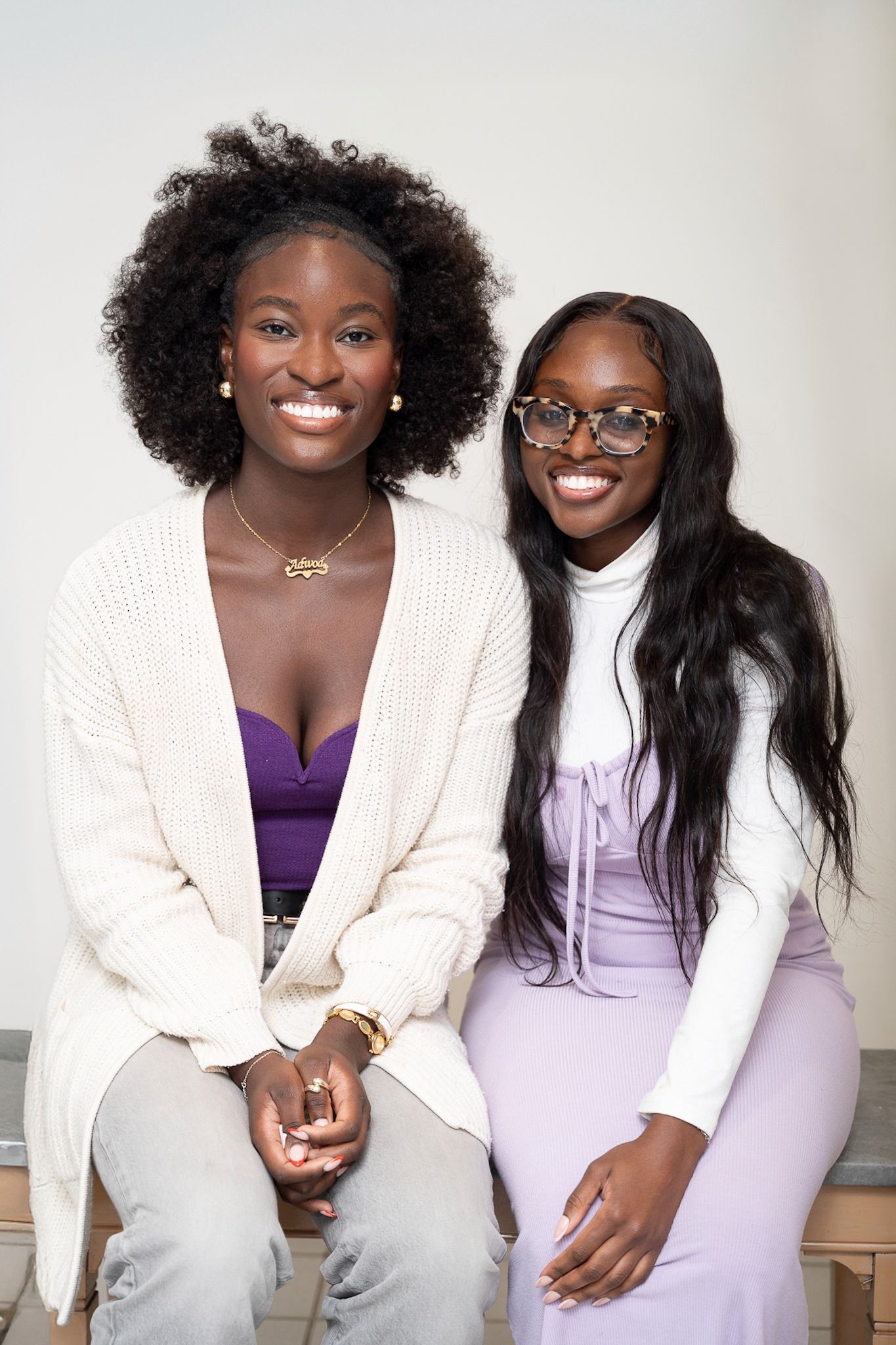Two people sitting together in coordinated white and purple outfits against light background.