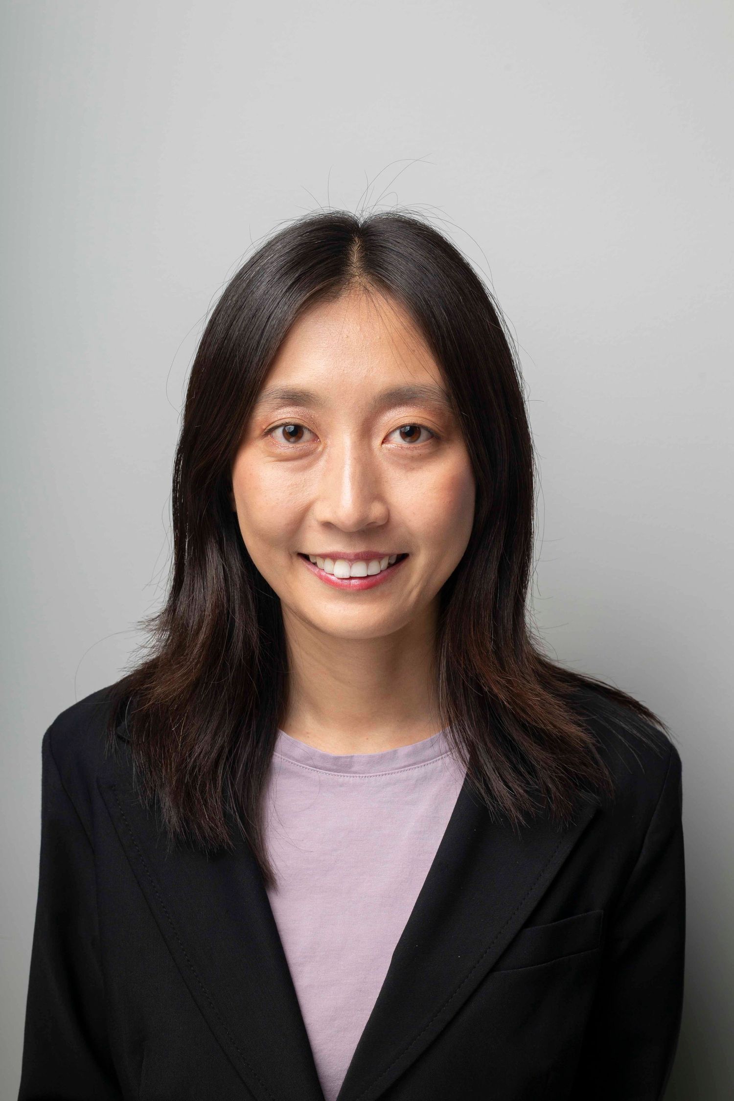 Professional headshot series showing different expressions while wearing a black blazer and lavender top against gray background.