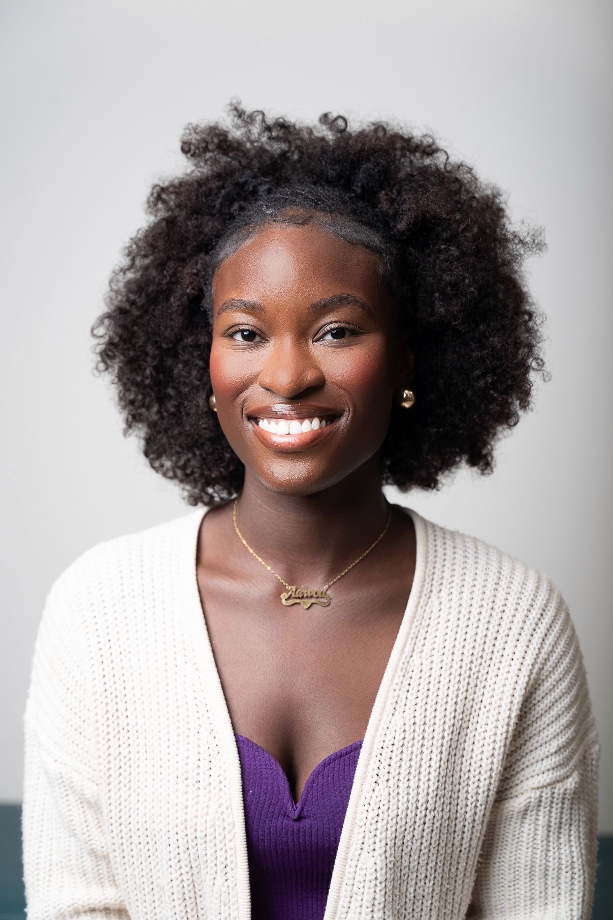 Portrait series showing person in white cardigan and purple top with natural curly hair.