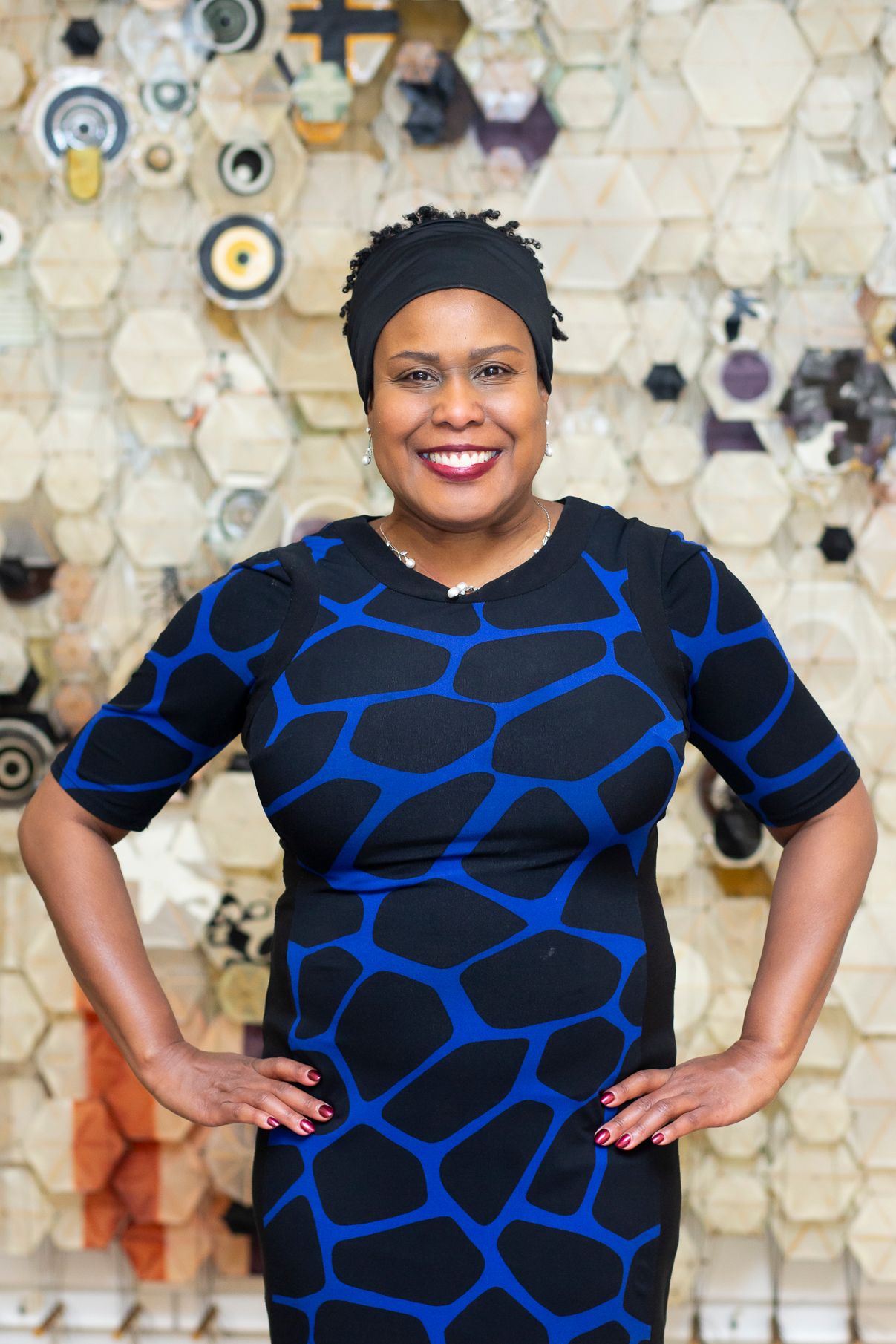 Portrait series in black and blue patterned dress against decorative hexagonal wall display.