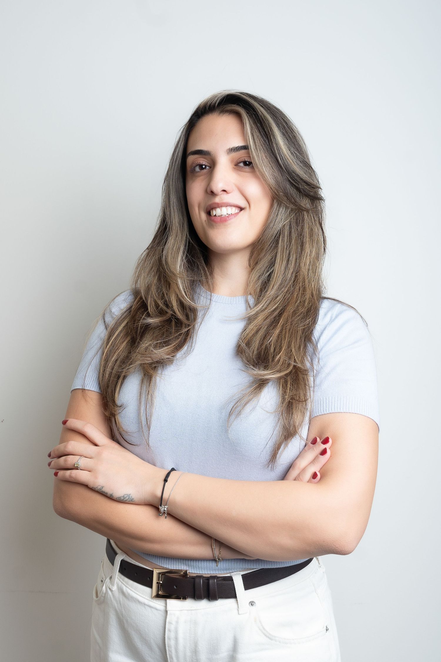 Person in white t-shirt and light jeans poses against white wall with natural brown hair flowing.