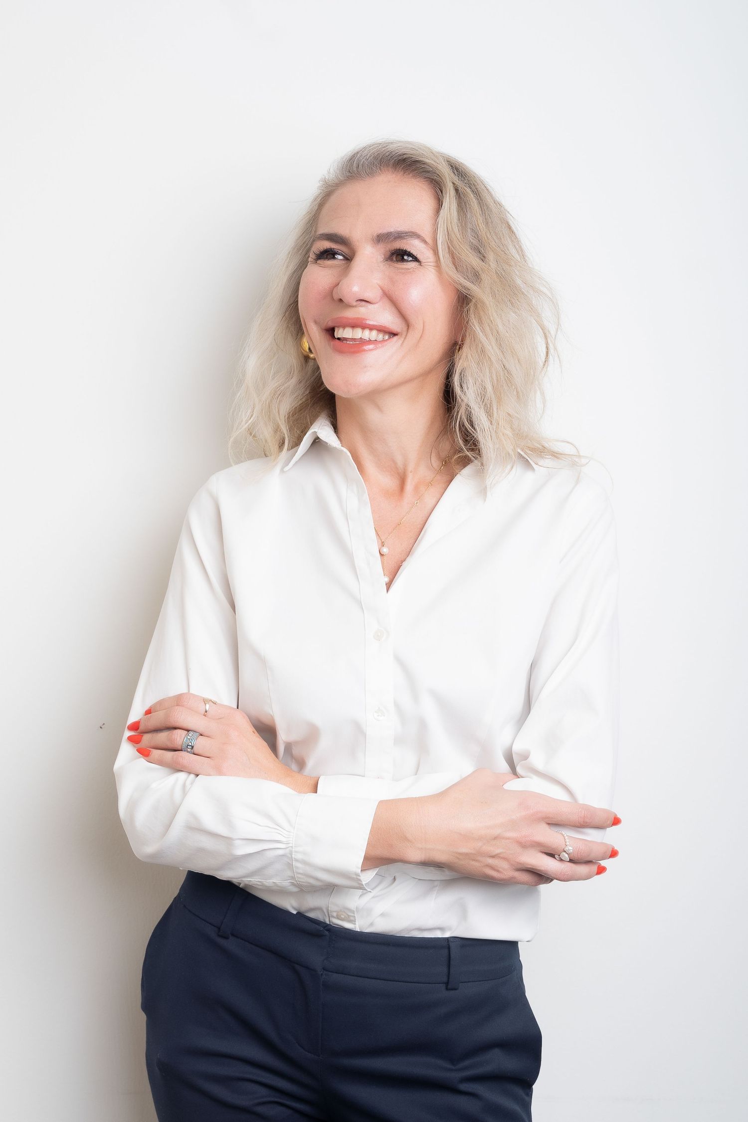 A person in a white button-down shirt and dark pants poses against a white wall in three different casual stances.
